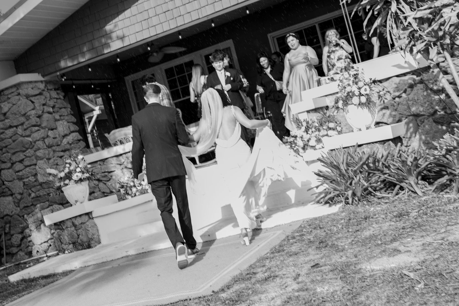 Black and white photo of a bride and groom walking hand in hand toward a venue entrance on their wedding day.