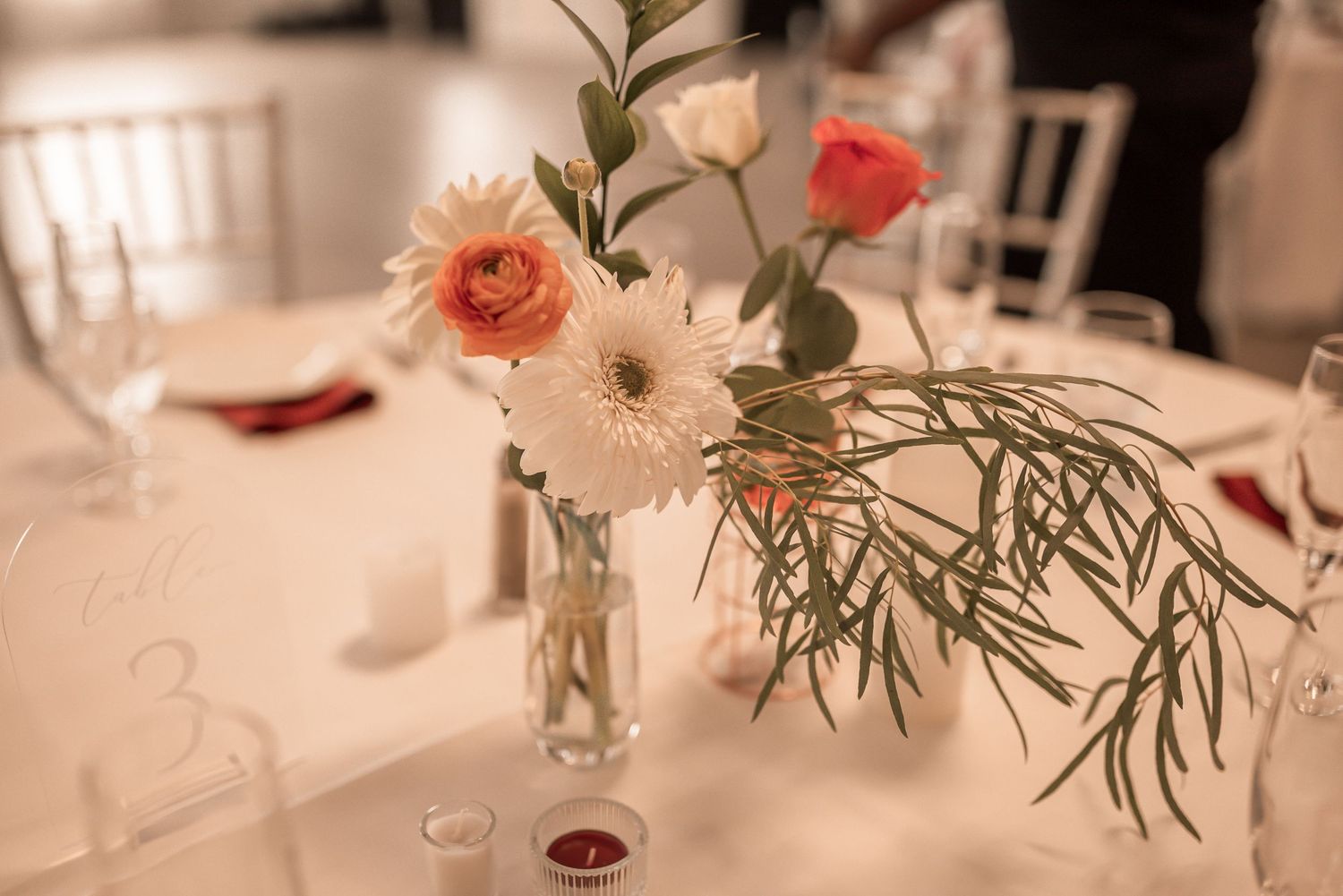 Elegant table setting with pink roses in small glass vases and white linens for a formal dinner event.