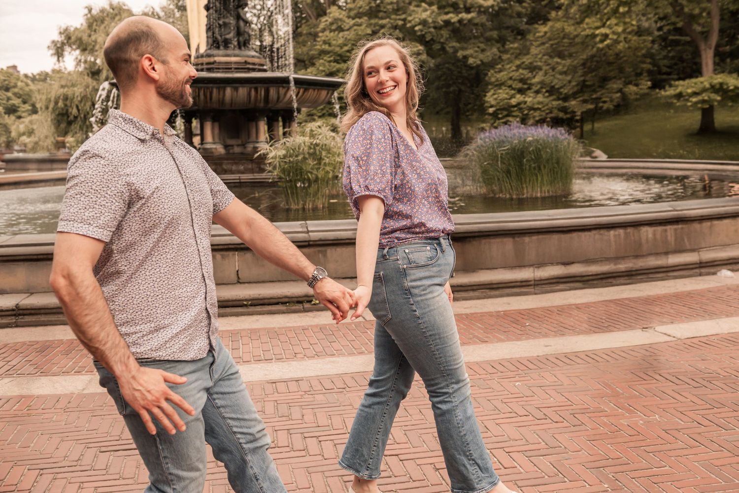 A couple holding hands and walking together on brick pavement in a park setting during golden hour.