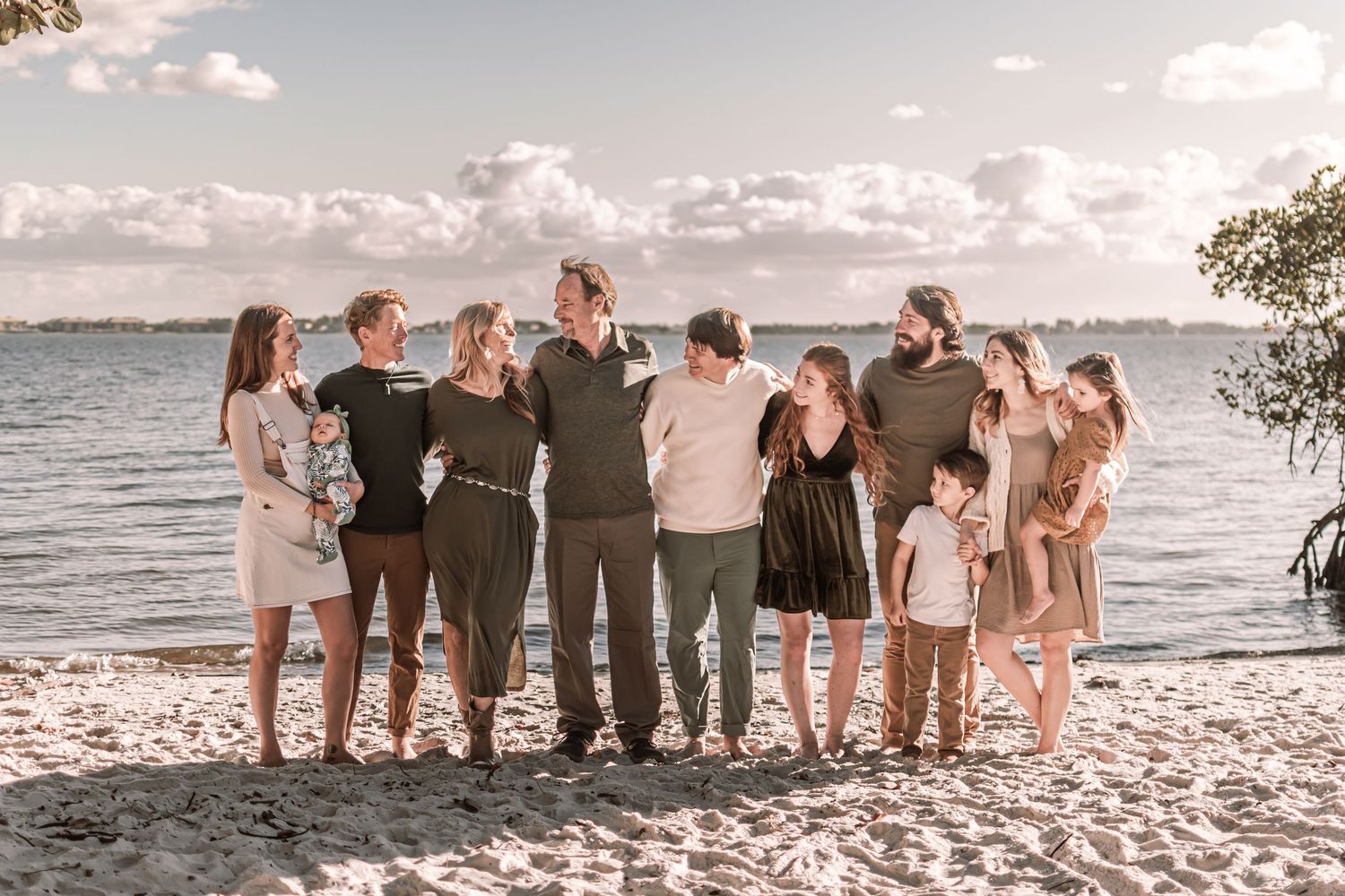 Group of friends standing together on a sandy beach at sunset overlooking a serene ocean view.