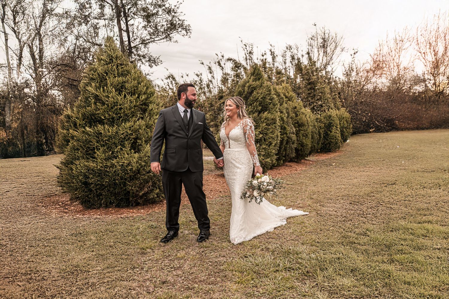 A couple walking through a natural field setting during an outdoor wedding photo session at sunset.