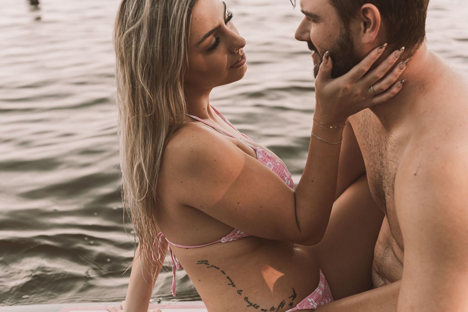 Romantic couple in swimwear sharing an intimate moment by the water, woman in pink bikini touching man's face.