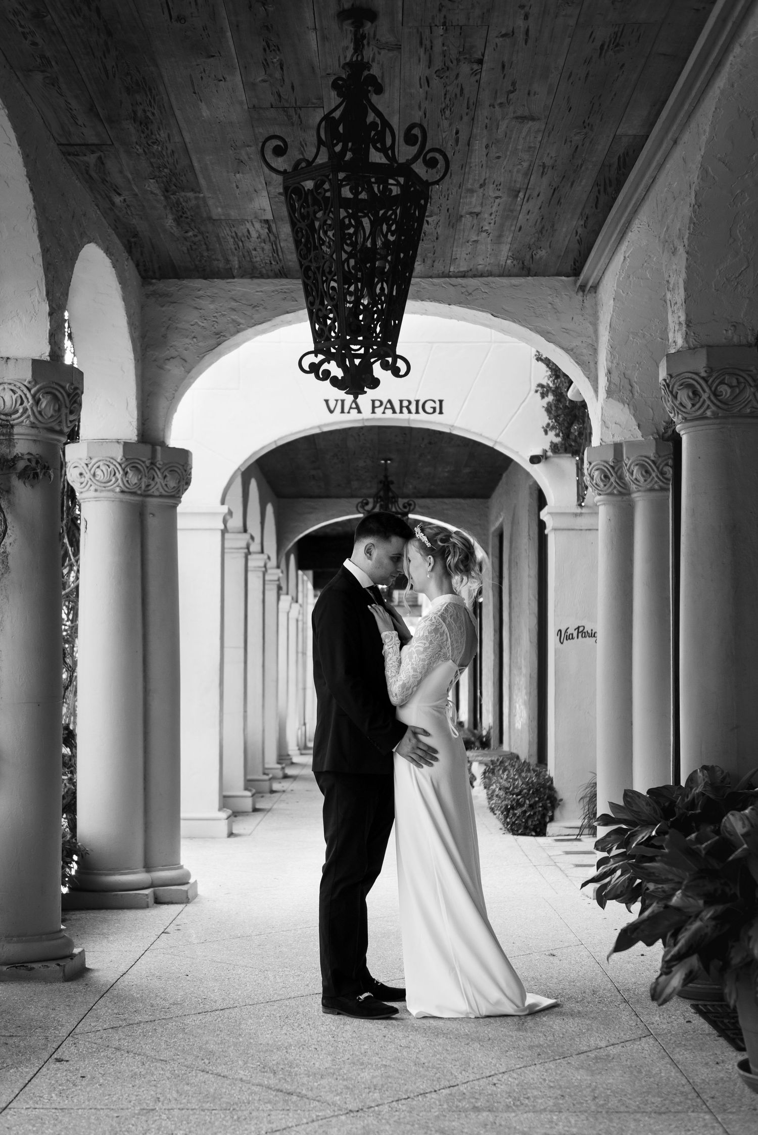 Black and white wedding photo of bride and groom embracing under arched colonnade at Via Parigi.