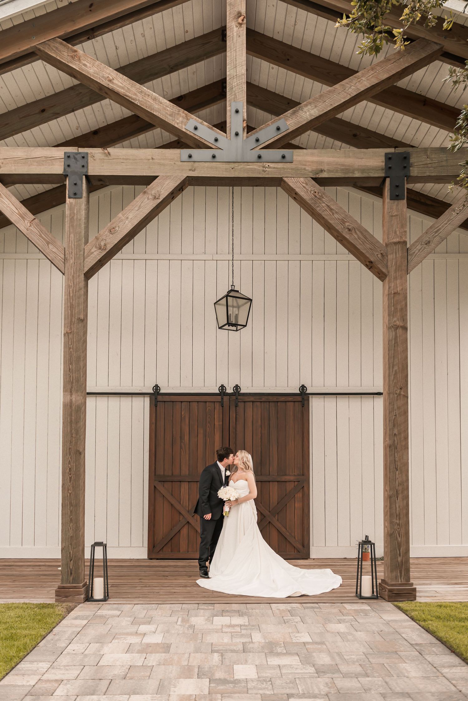 Bride and groom share a kiss under rustic wooden beams at a barn wedding venue with sliding doors.