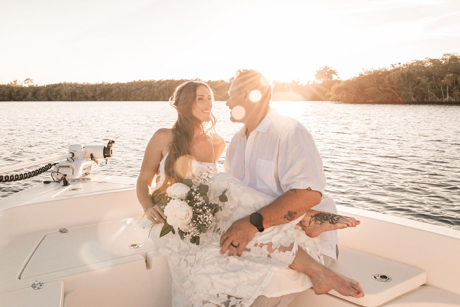 A couple embraces on a boat deck during sunset over a tranquil lake, creating a romantic silhouette against the golden sky.