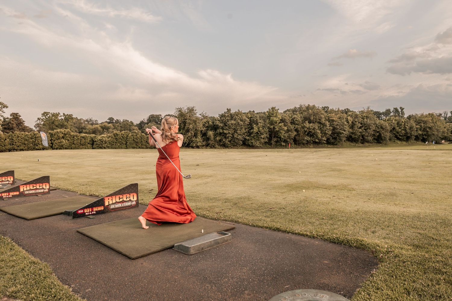 Person wearing red jumpsuit performs freestyle motocross jump sequence on dirt ramps at outdoor track.