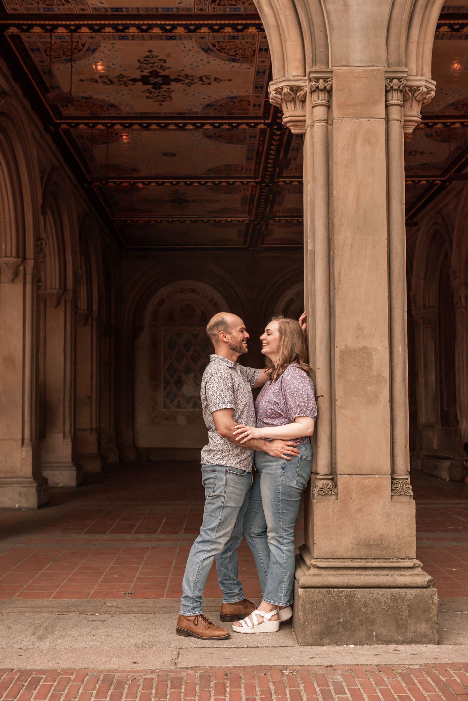 A couple embraces under ornate stone archways in a historic architectural passageway.
