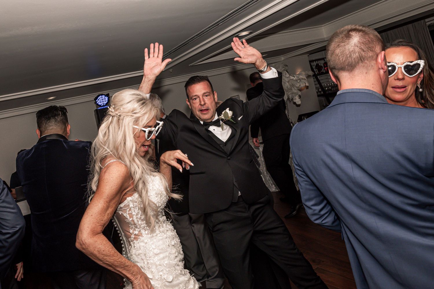 Wedding guests dance and celebrate energetically on the dance floor at an indoor reception party.