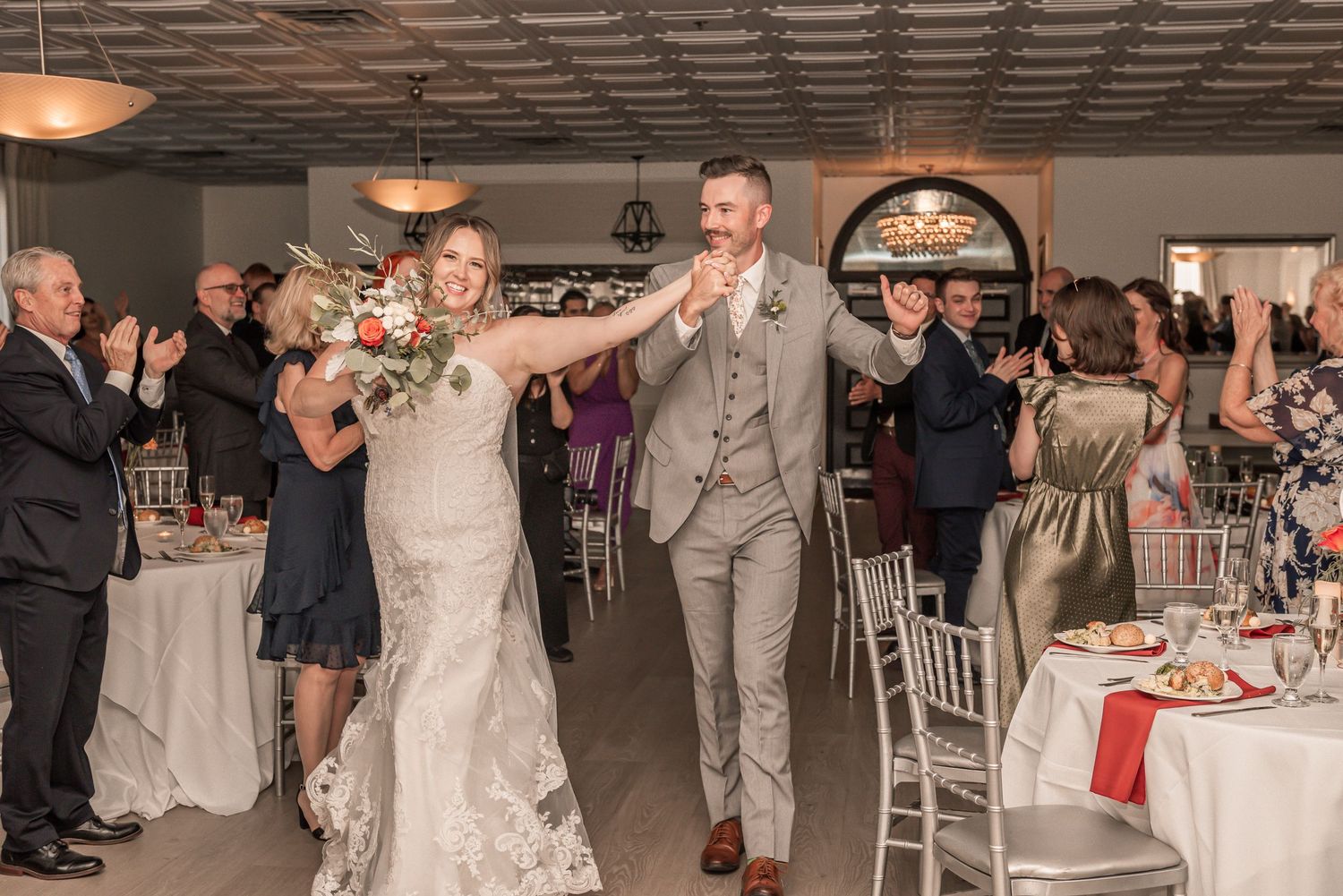 A wedding couple makes their grand entrance into an elegant reception hall filled with celebrating guests.