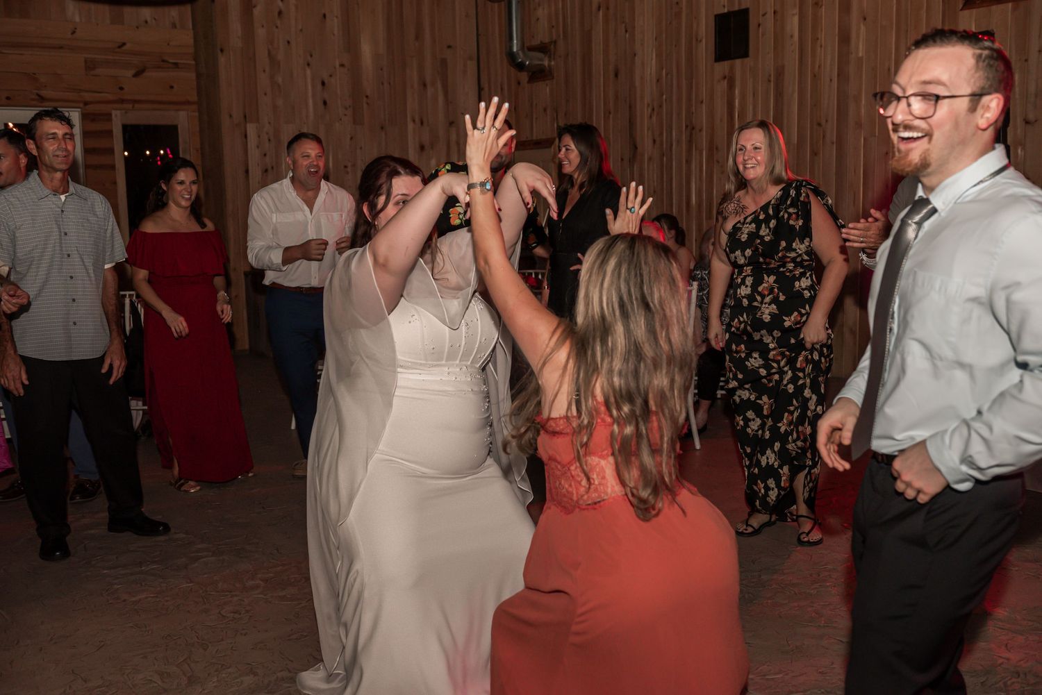 People dancing and socializing at a rustic barn wedding reception with wooden walls and warm lighting.