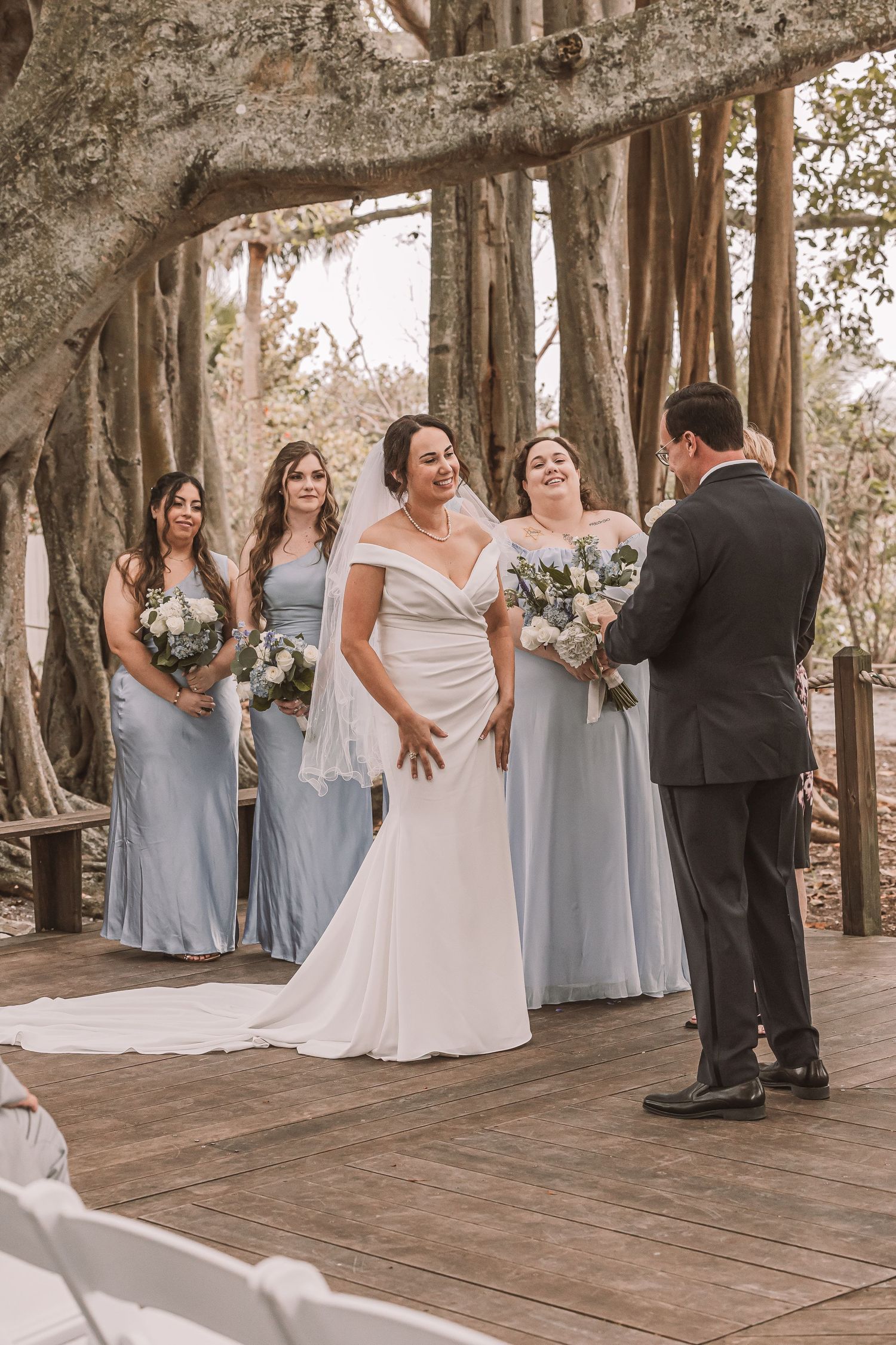 Wedding party poses for candid photos on a rustic wooden deck surrounded by trees at an outdoor venue.