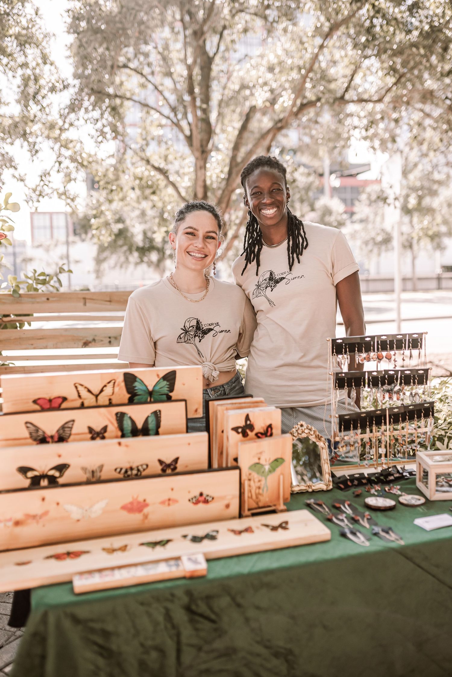 Local artisans display their handmade butterfly artwork and jewelry collection at an outdoor market table.