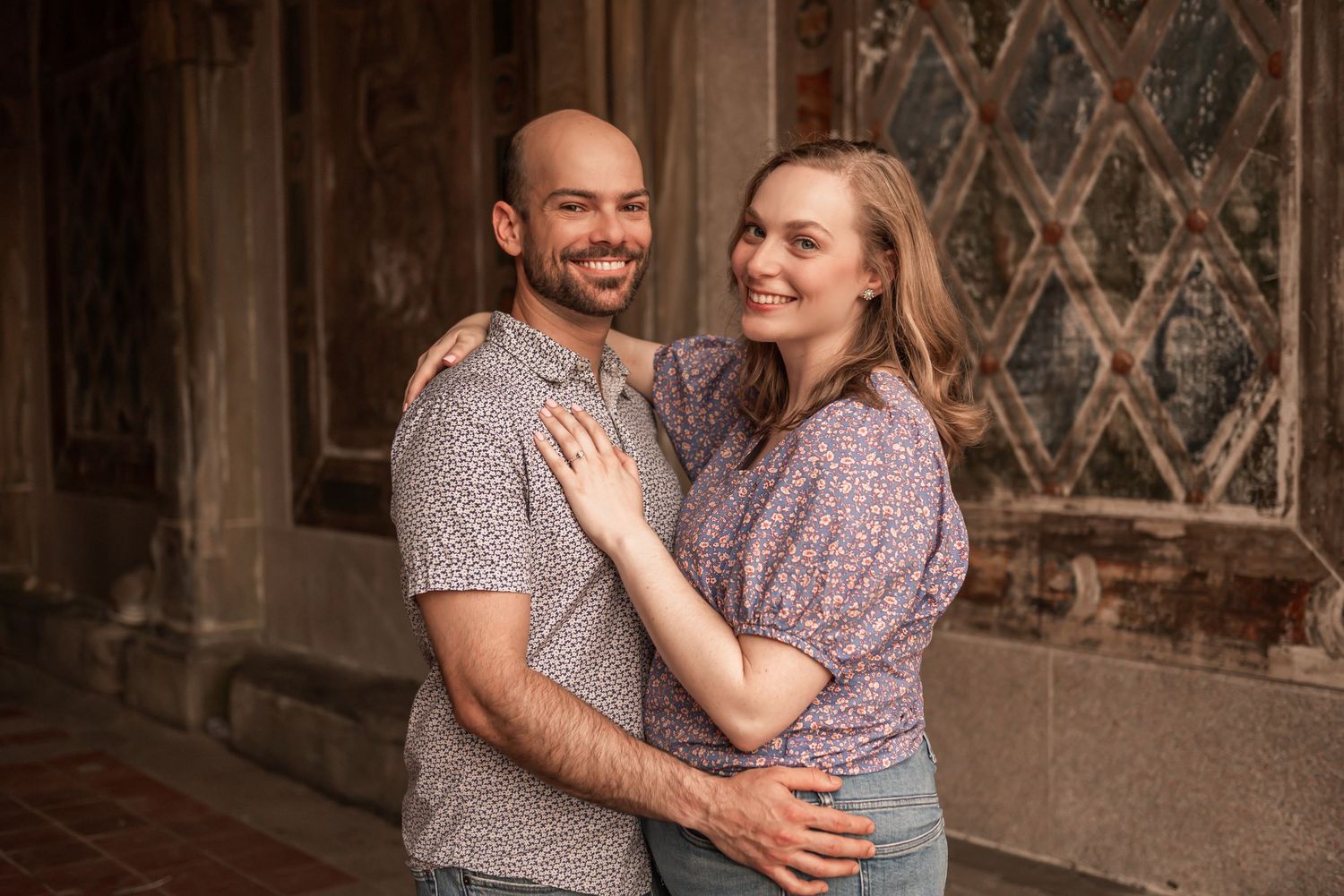 Two people embrace and laugh together in a romantic engagement photo session against an ornate stone building.