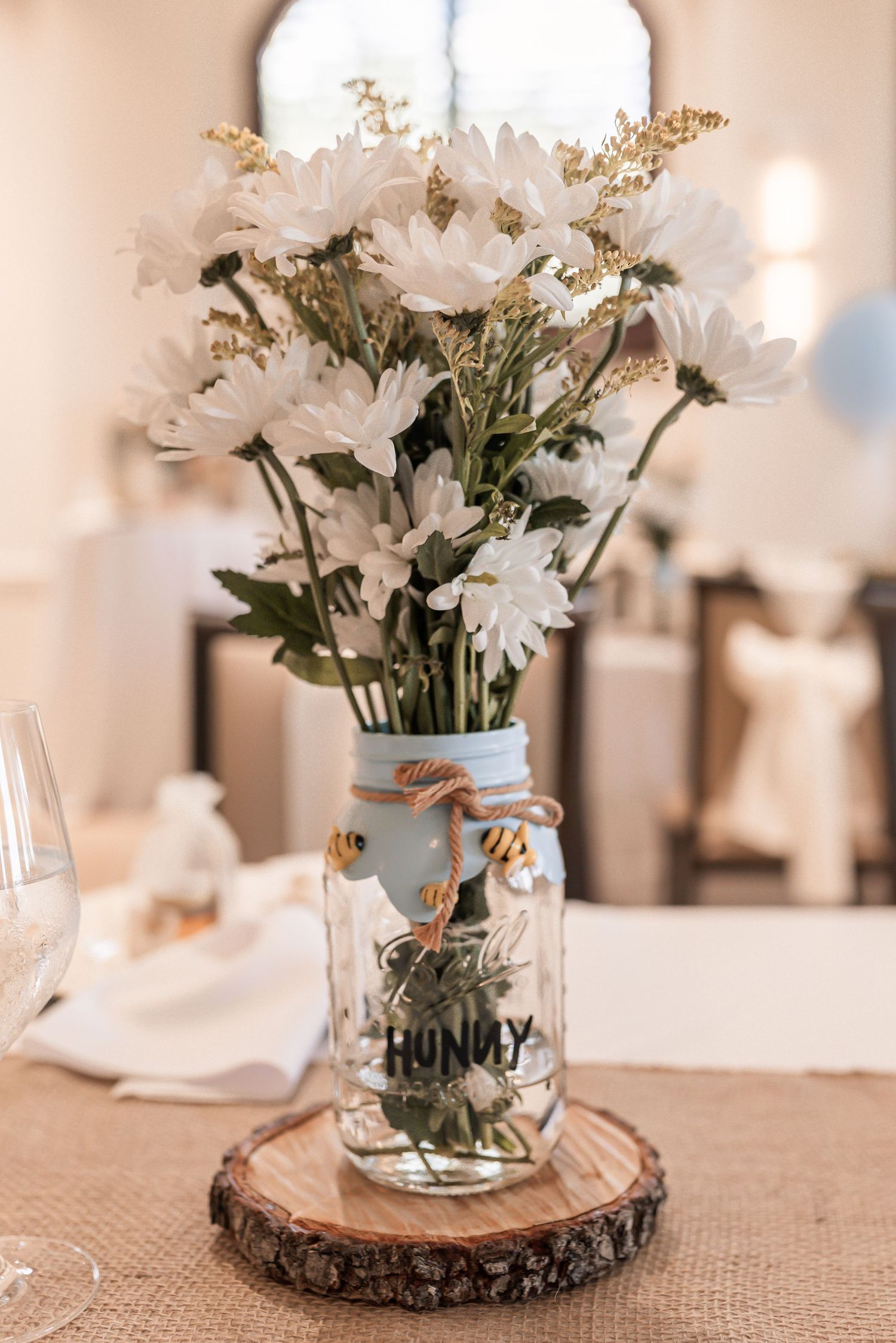 White floral centerpieces in glass vases displayed on rustic wood slices with burlap accents.