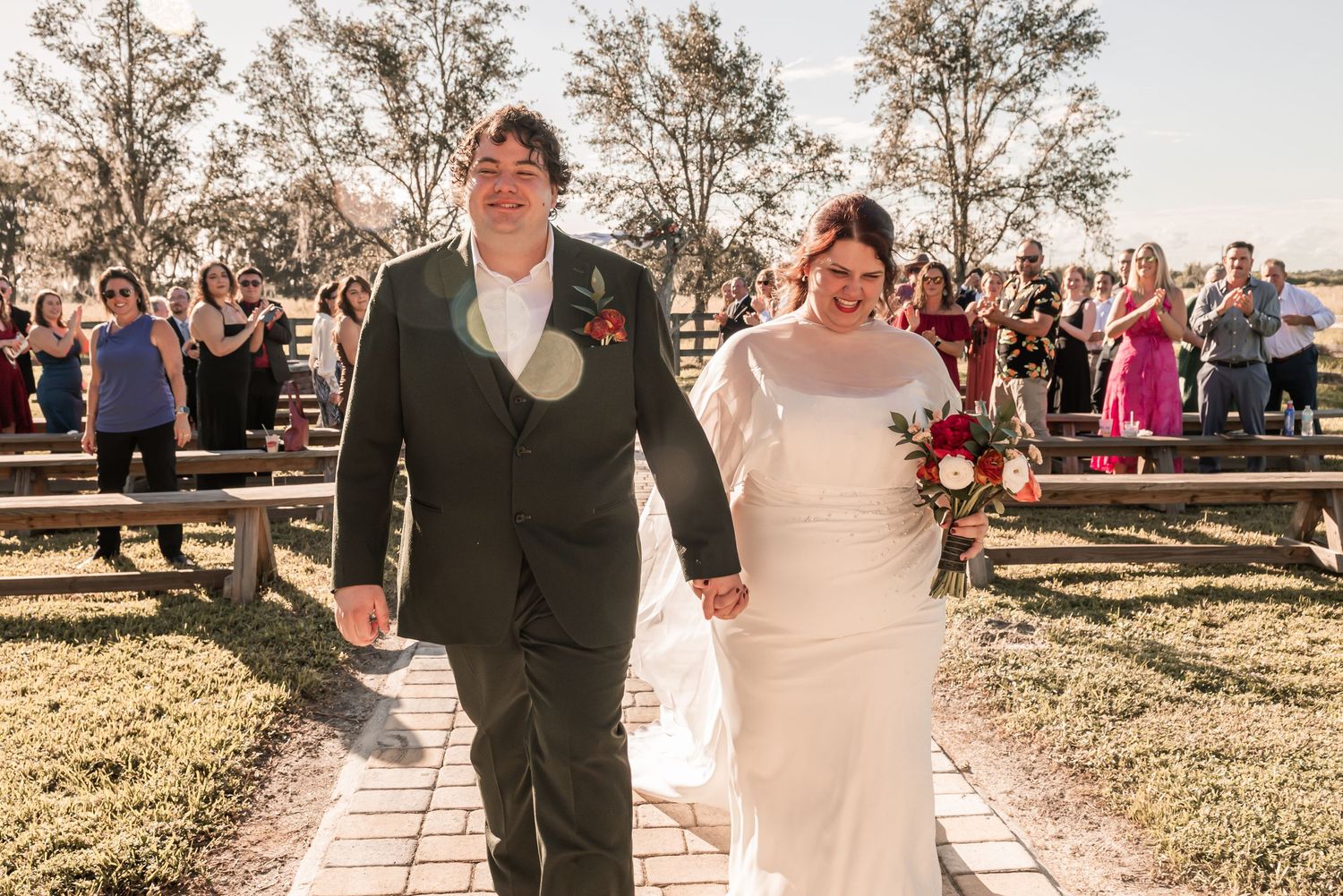 A joyful couple walks down an outdoor aisle at their wedding ceremony as guests celebrate their special moment.