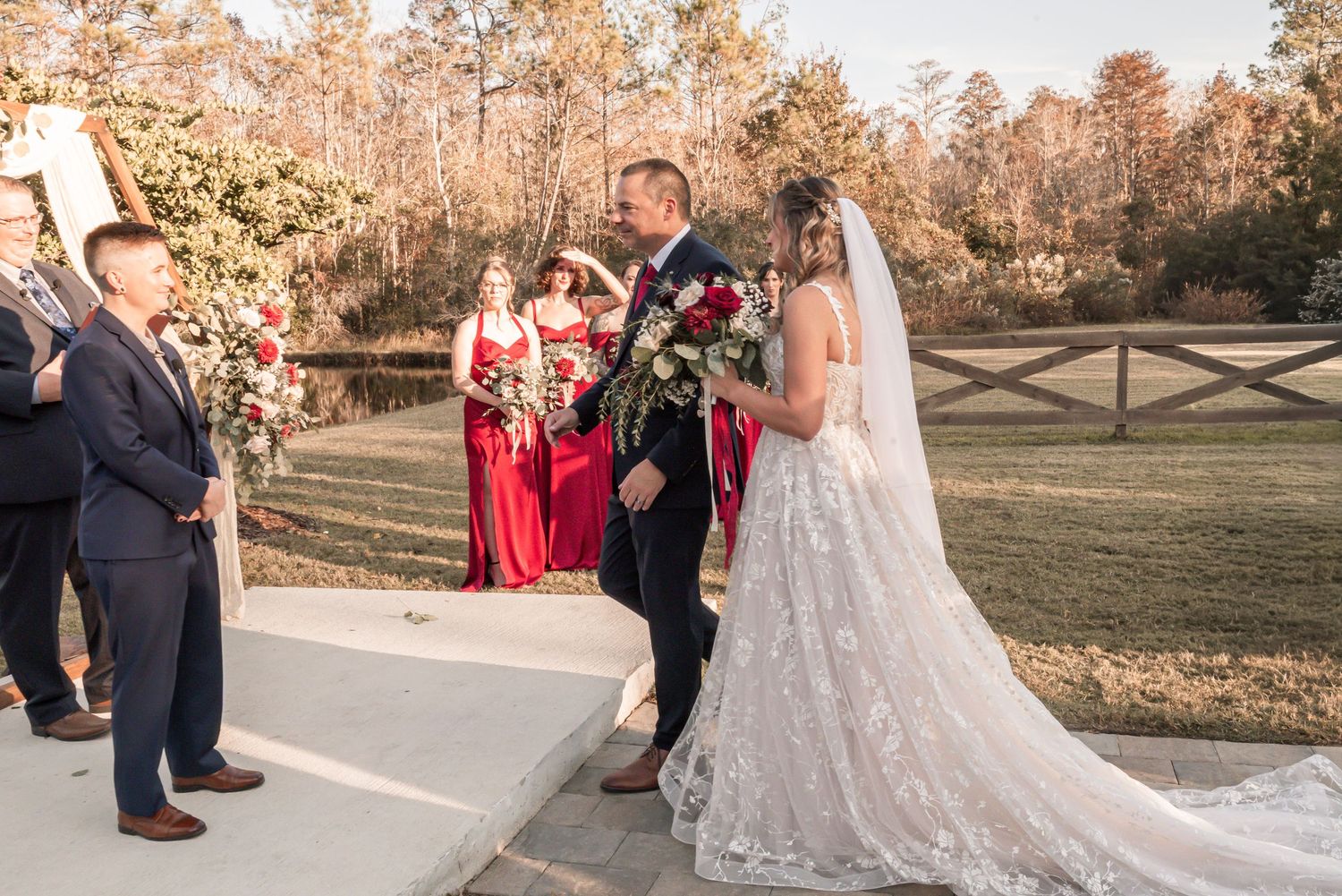 Wedding party stands on a paved pathway surrounded by autumn trees during outdoor ceremony at sunset.