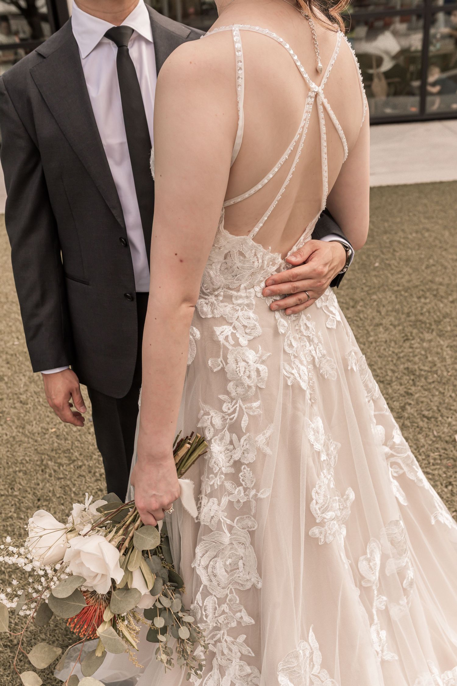 Close-up details of a romantic wedding dress featuring delicate lace appliques and sheer straps against a garden backdrop.