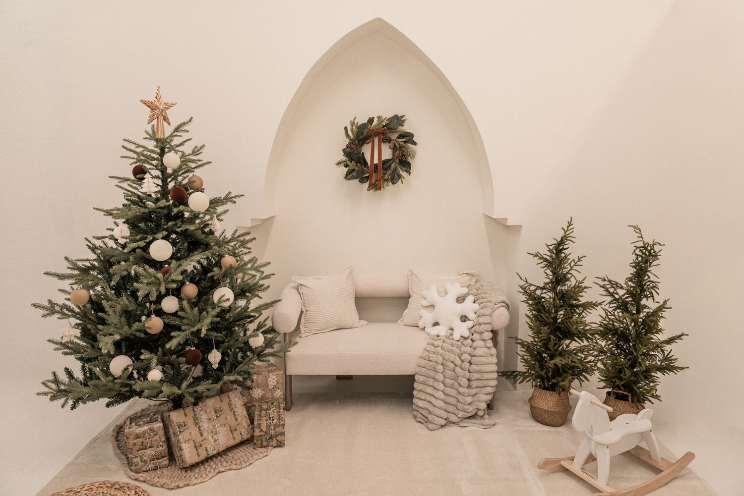 Minimalist Christmas decor featuring small evergreen trees and rustic decorations against a white wall.