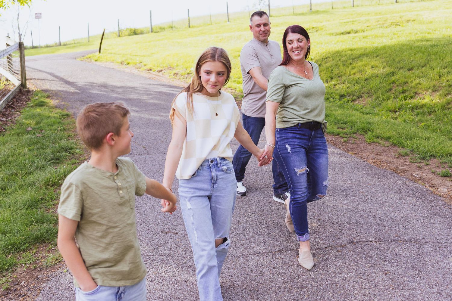 Four people walk together down a paved path surrounded by green grass on a sunny day.