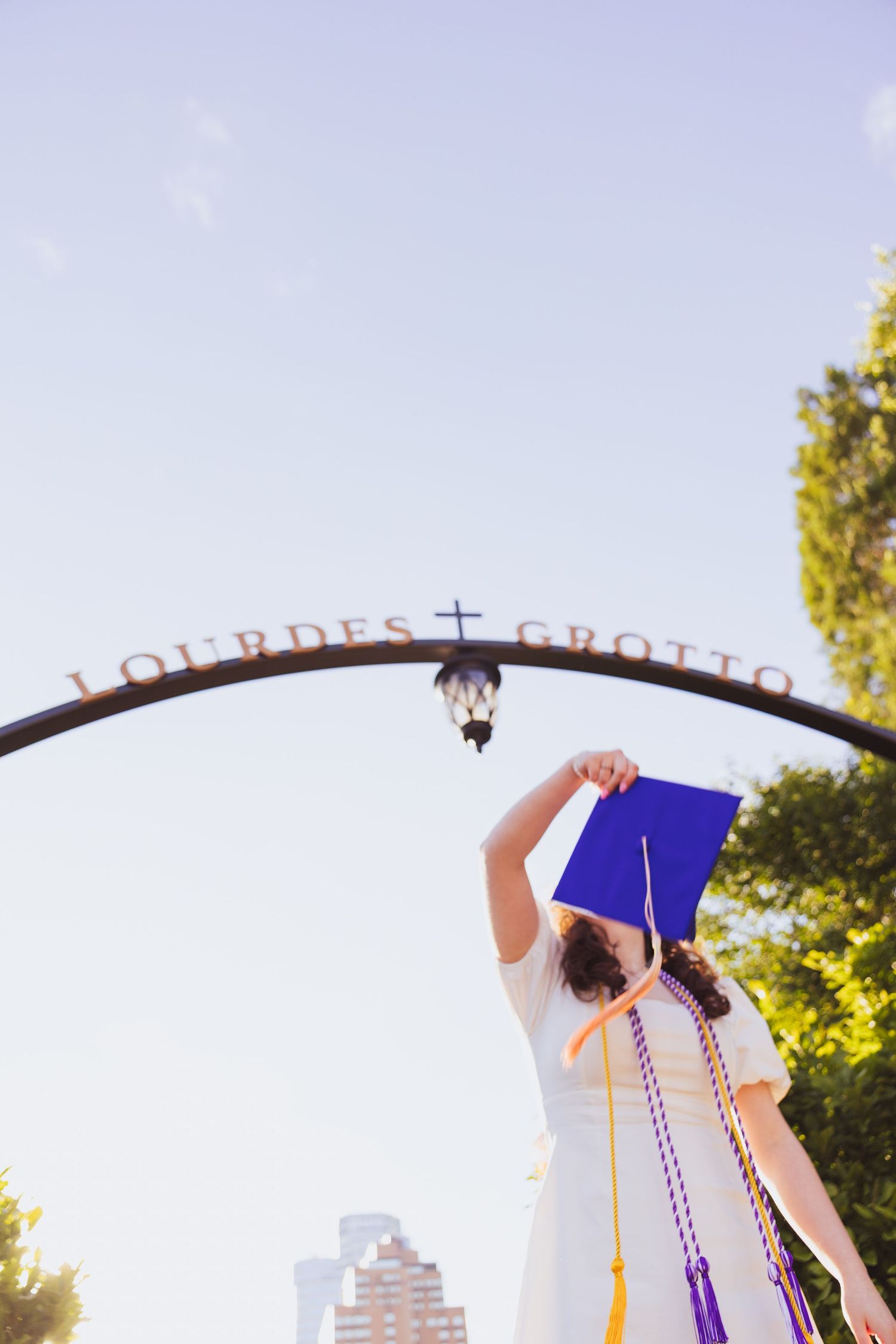 Graduates raise their diplomas against a blue sky during an outdoor graduation ceremony celebration.