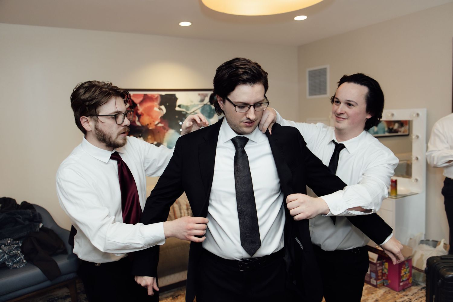 Three men in formal attire helping each other get dressed for a wedding or special occasion.