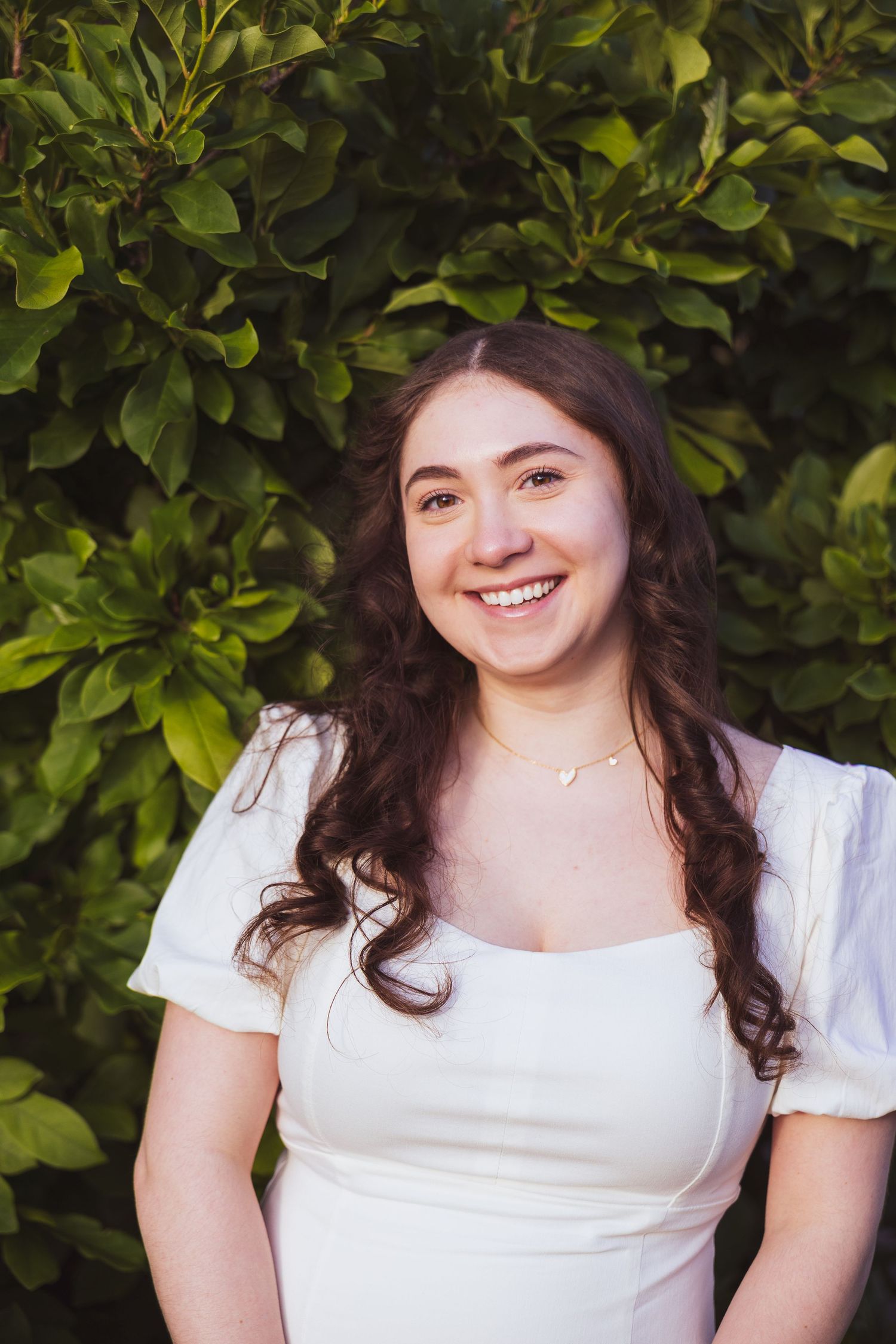 Four outdoor portraits of a person in a white dress with dark hair smiling against a leafy green background.