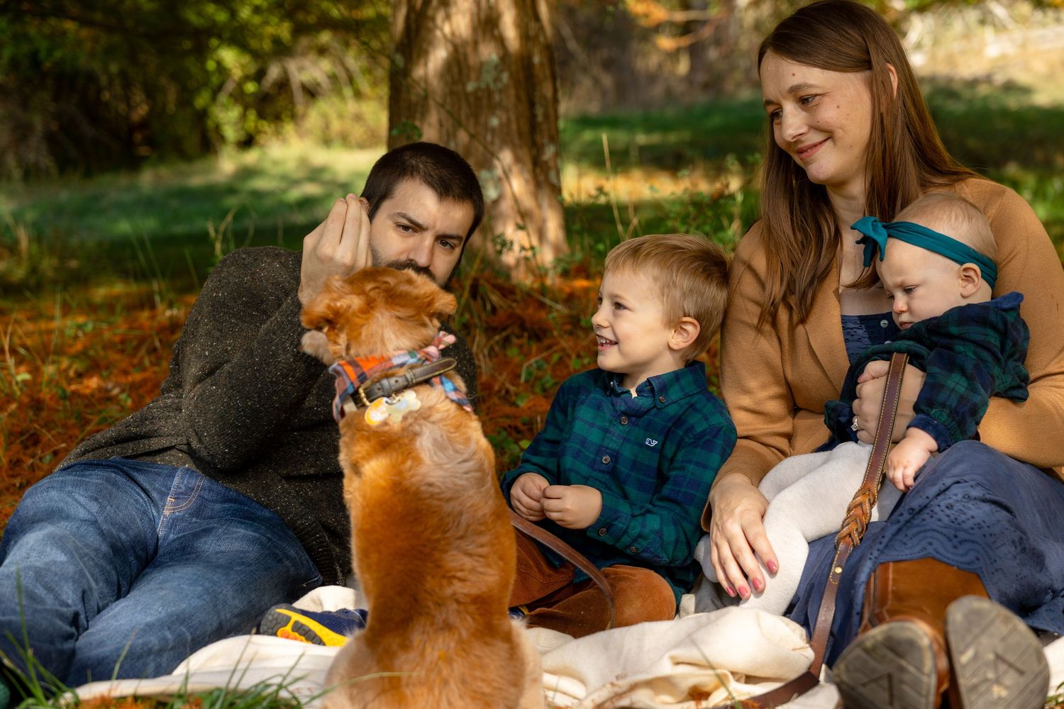 Family with two young children and a golden dog enjoying a picnic in an autumn park setting.