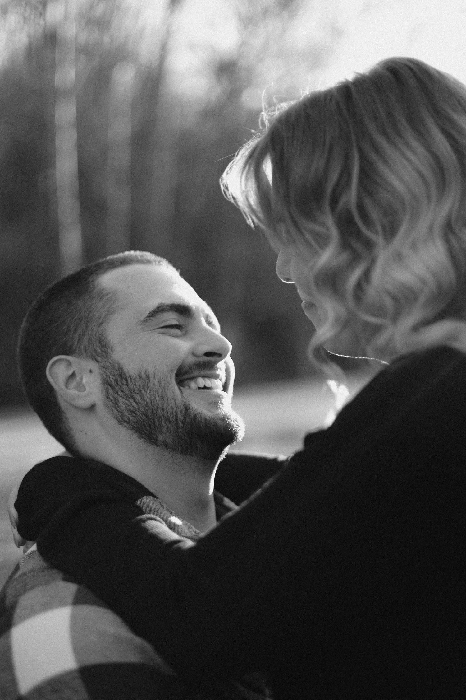 Intimate black and white portrait of couple laughing together in natural setting.