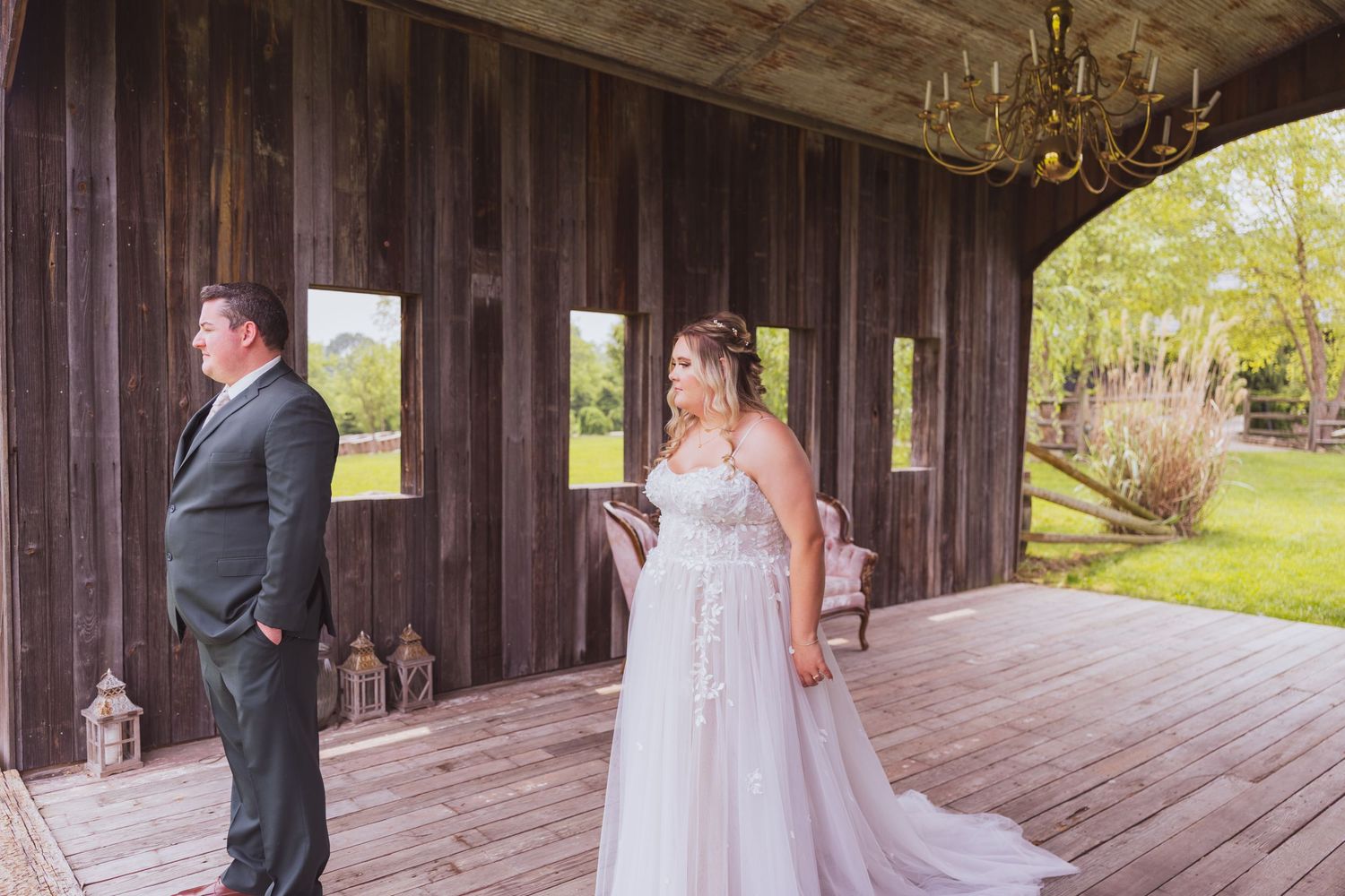 A wedding couple shares their first look moment on a rustic wooden porch with a chandelier overhead.