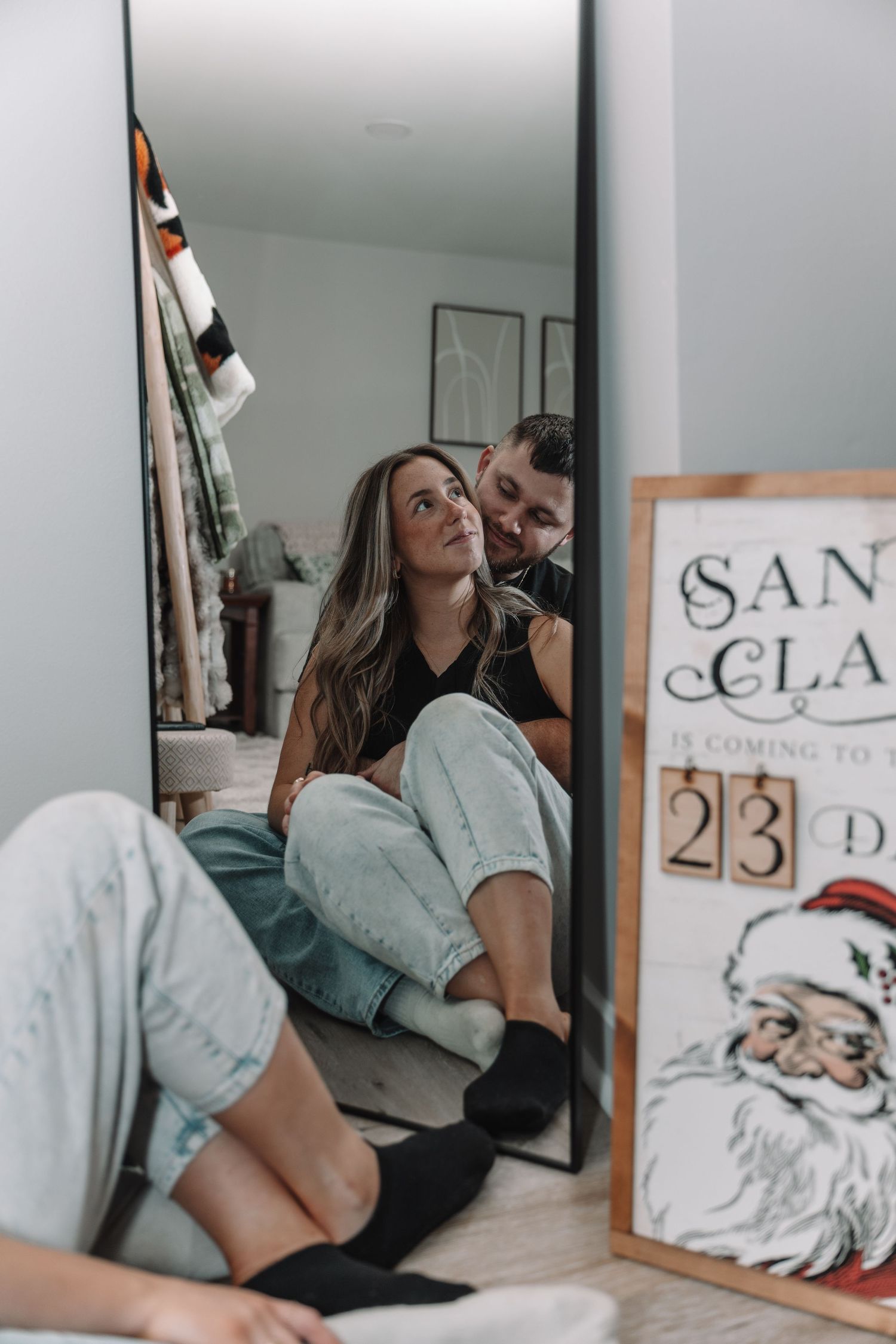 Couple sitting on floor reflected in mirror near Santa Claus countdown sign showing 23 days until Christmas.