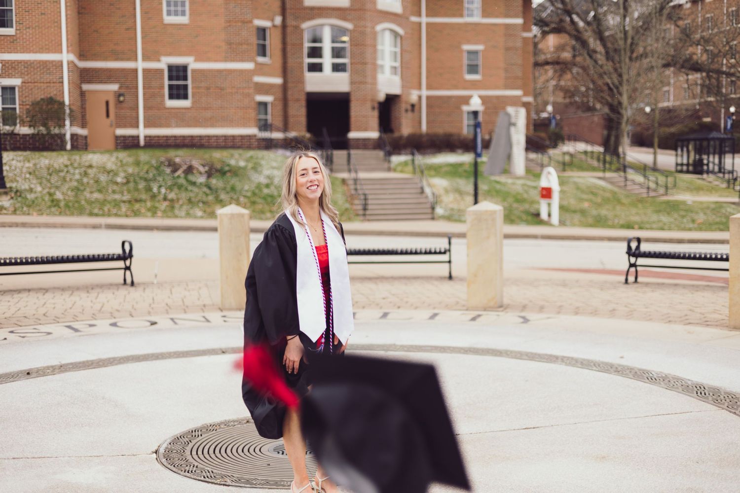 Graduate in black gown celebrating on campus circular courtyard.