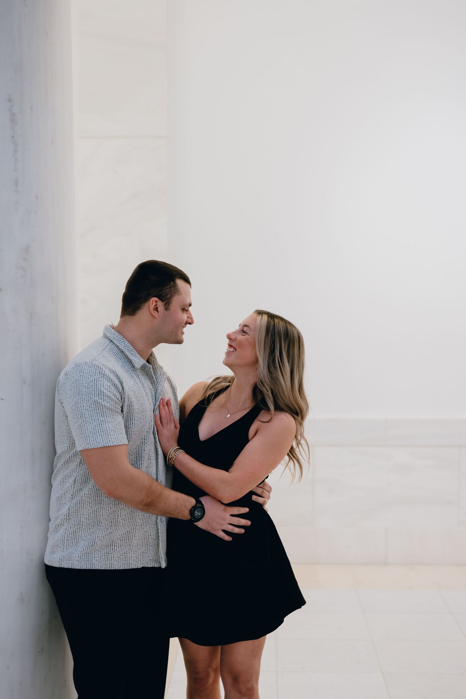 Romantic couple sharing laughter while embracing against white wall.