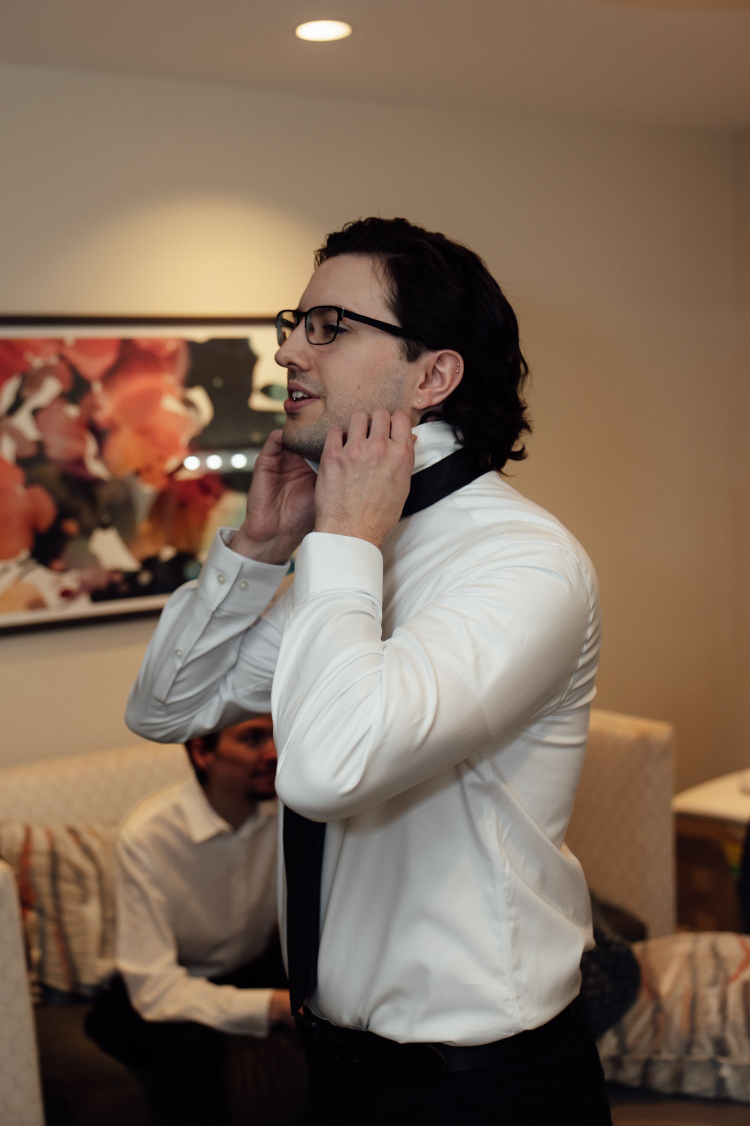 Man in white shirt and glasses adjusting his tie while getting dressed for a formal event.