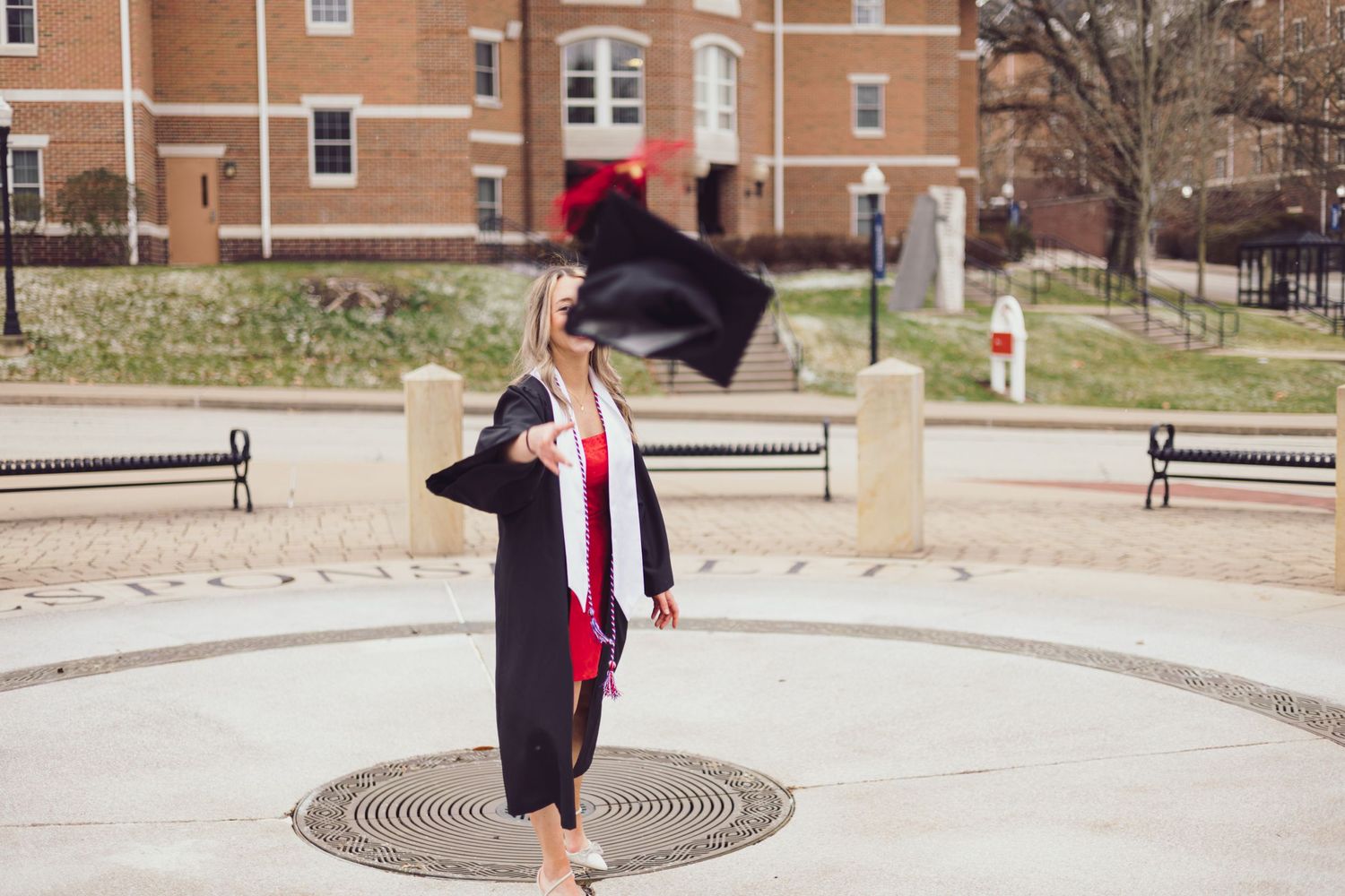 Graduate throwing graduation cap in air on university campus.