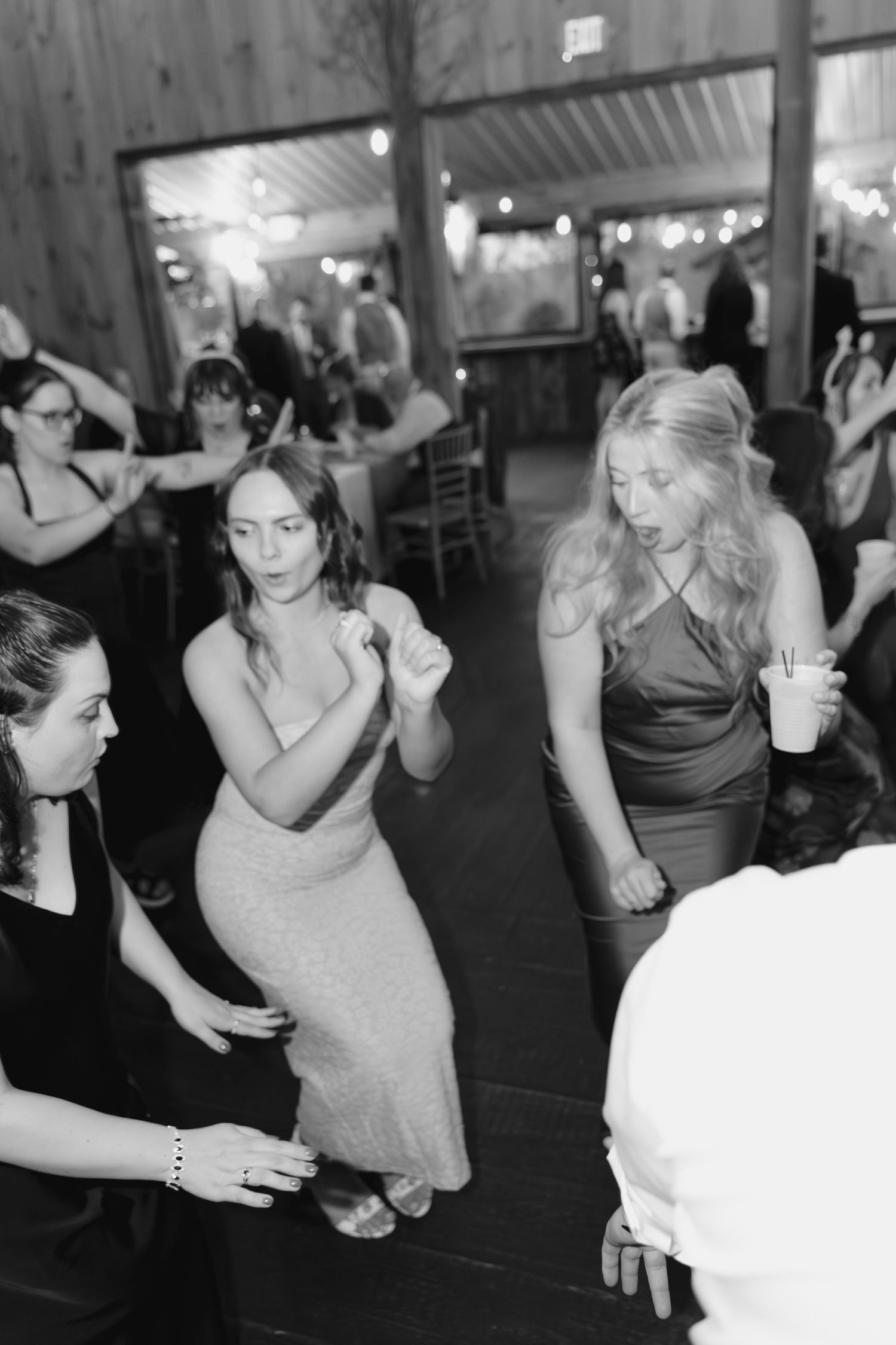 Guests dancing joyfully at a wedding reception in a rustic barn venue, captured in black and white photography.