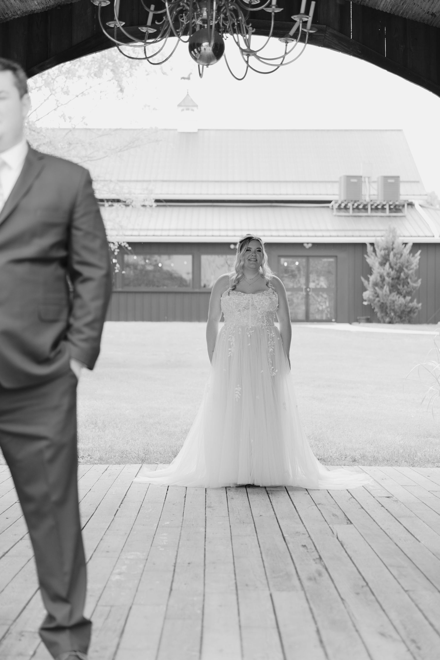 Black and white wedding photo showing the bottom half of a bride in a white dress and groom in dark suit on wooden deck.