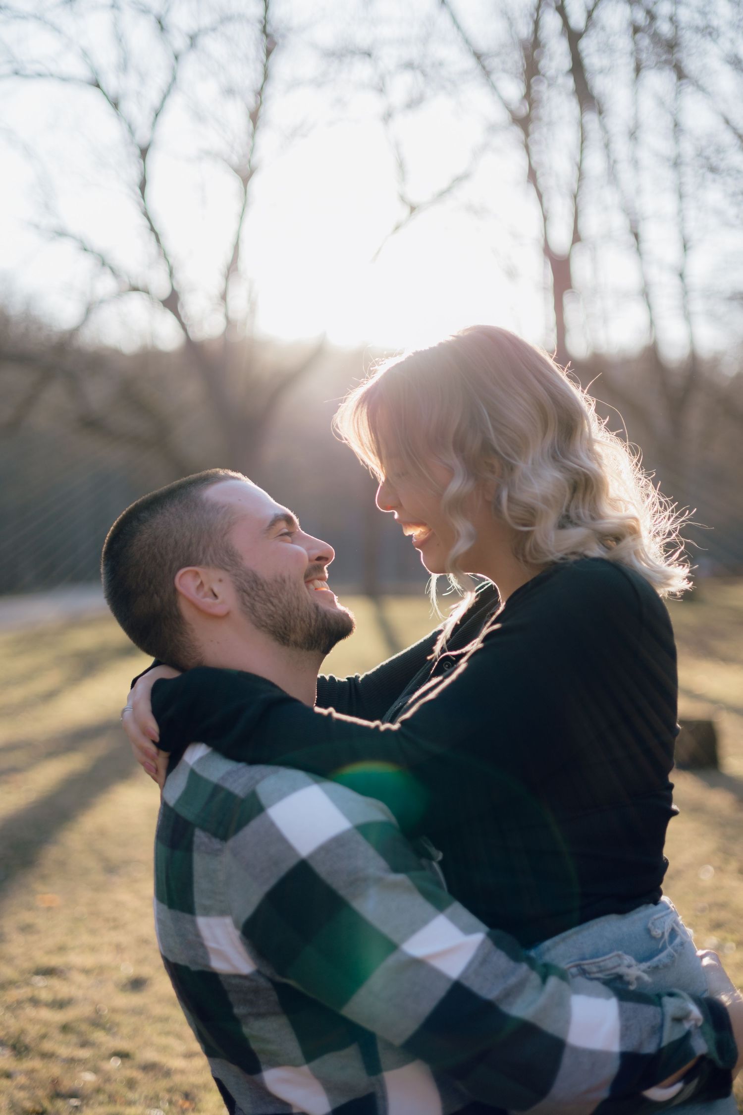 Romantic couple embracing outdoors during golden hour with sunlit trees in background.