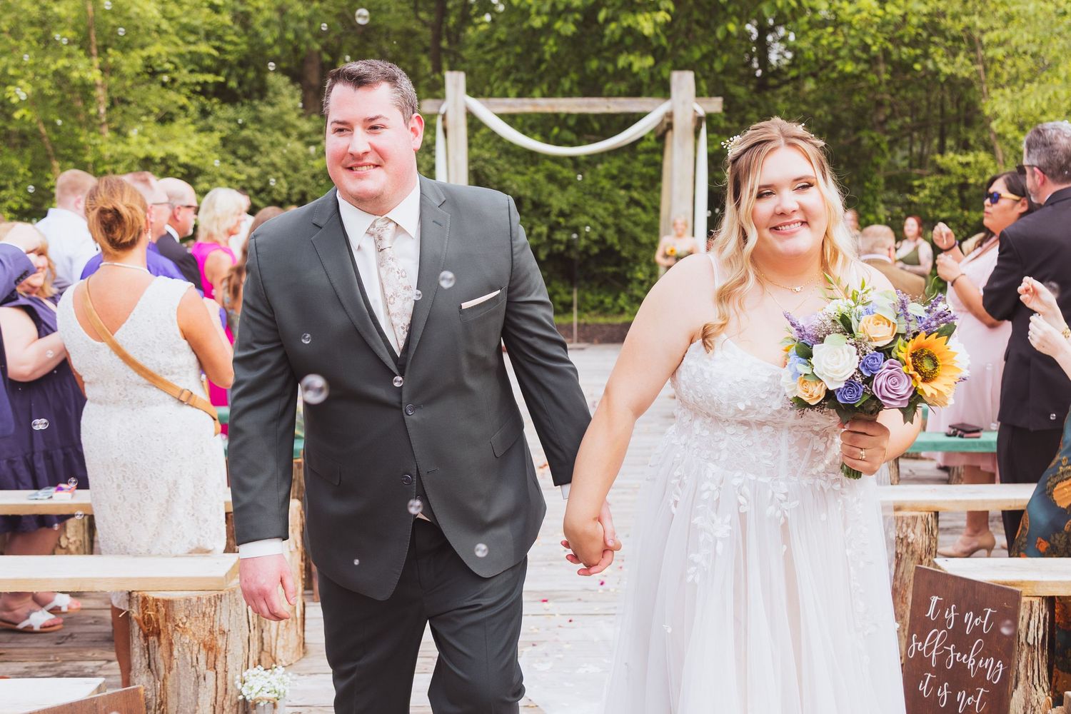 Outdoor wedding ceremony with floral decorations and guests gathered at a scenic garden venue.
