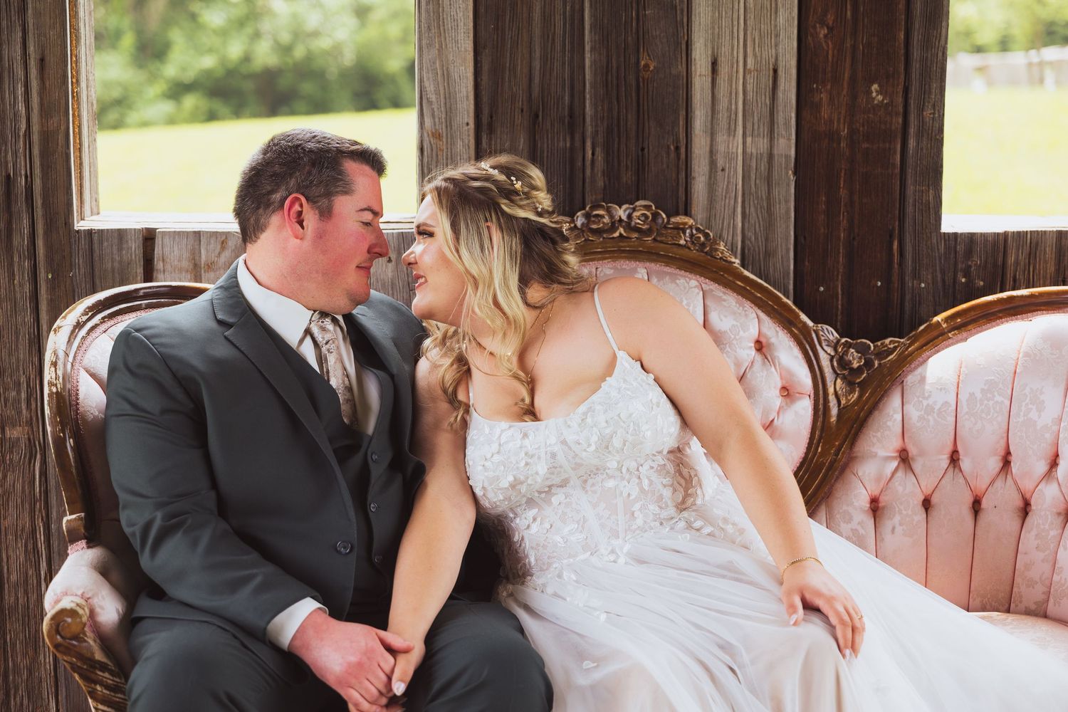 Romantic wedding couple sharing tender moments on vintage furniture in rustic barn setting.