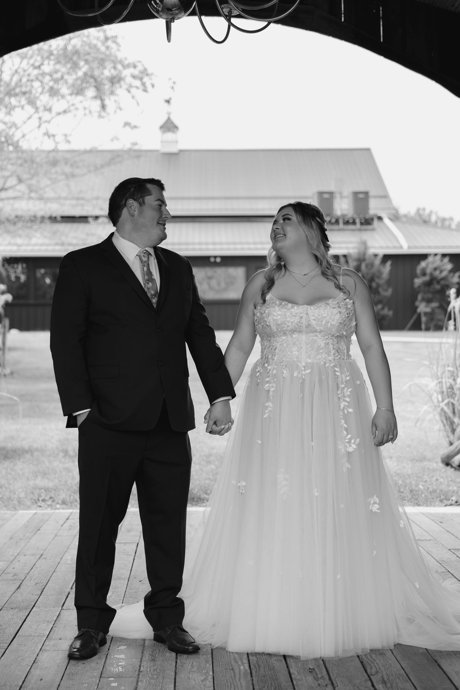 Black and white photo of newlyweds sharing a tender moment under a covered wooden walkway.