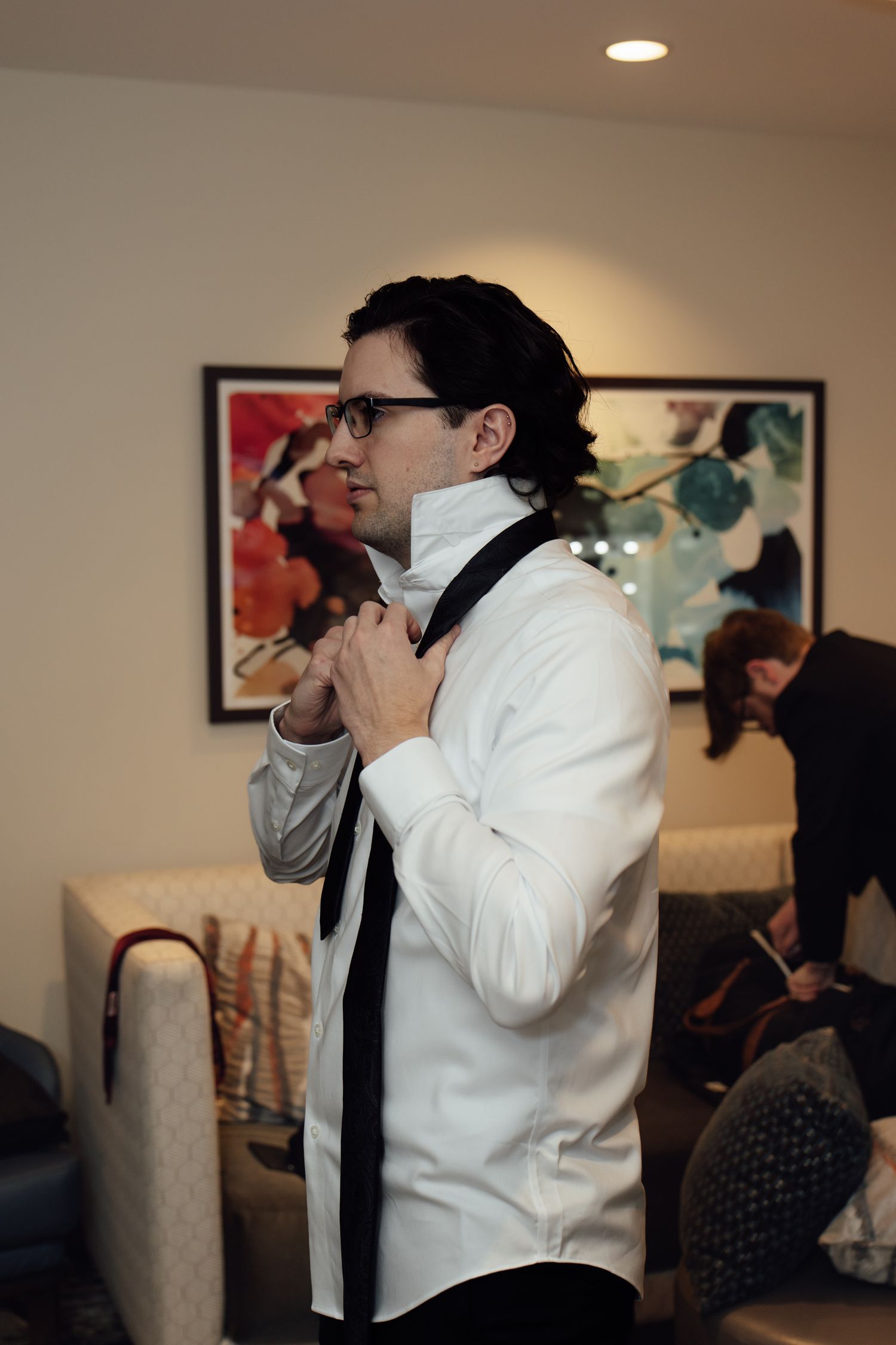 Groom in white shirt adjusting black tie while getting ready for wedding ceremony in elegant room.