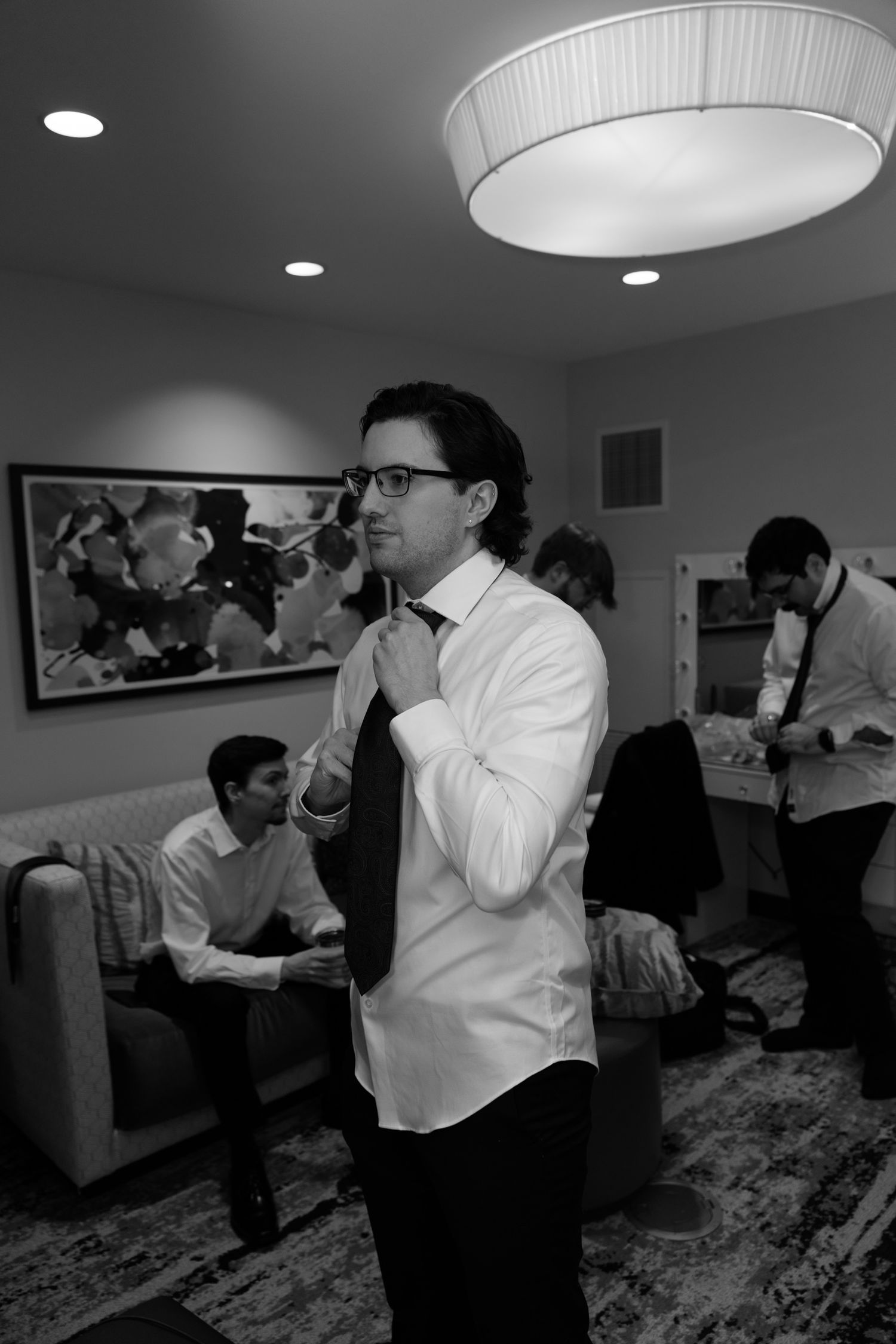 Black and white photo of groom fixing tie surrounded by groomsmen getting ready for wedding.