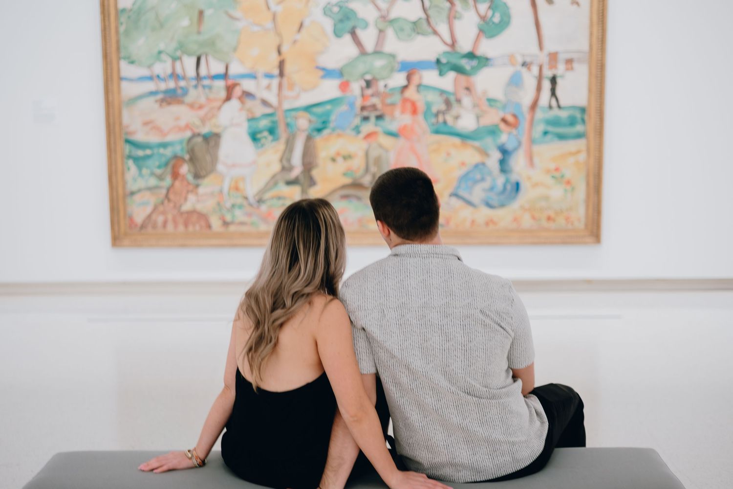 Couple sitting on bench admiring colorful impressionist painting in art museum gallery.
