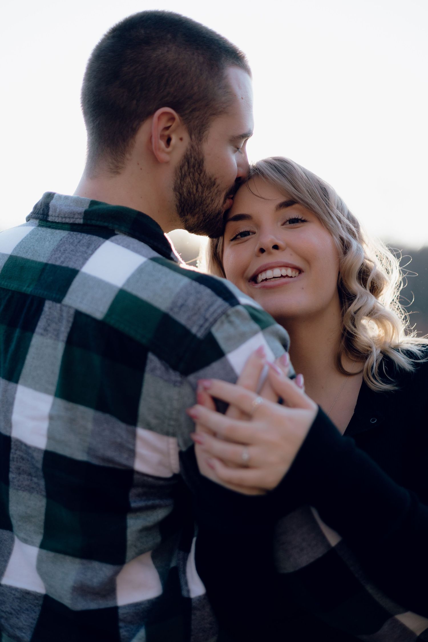 Couple sharing intimate moment outdoors wearing plaid shirt and black sweater.