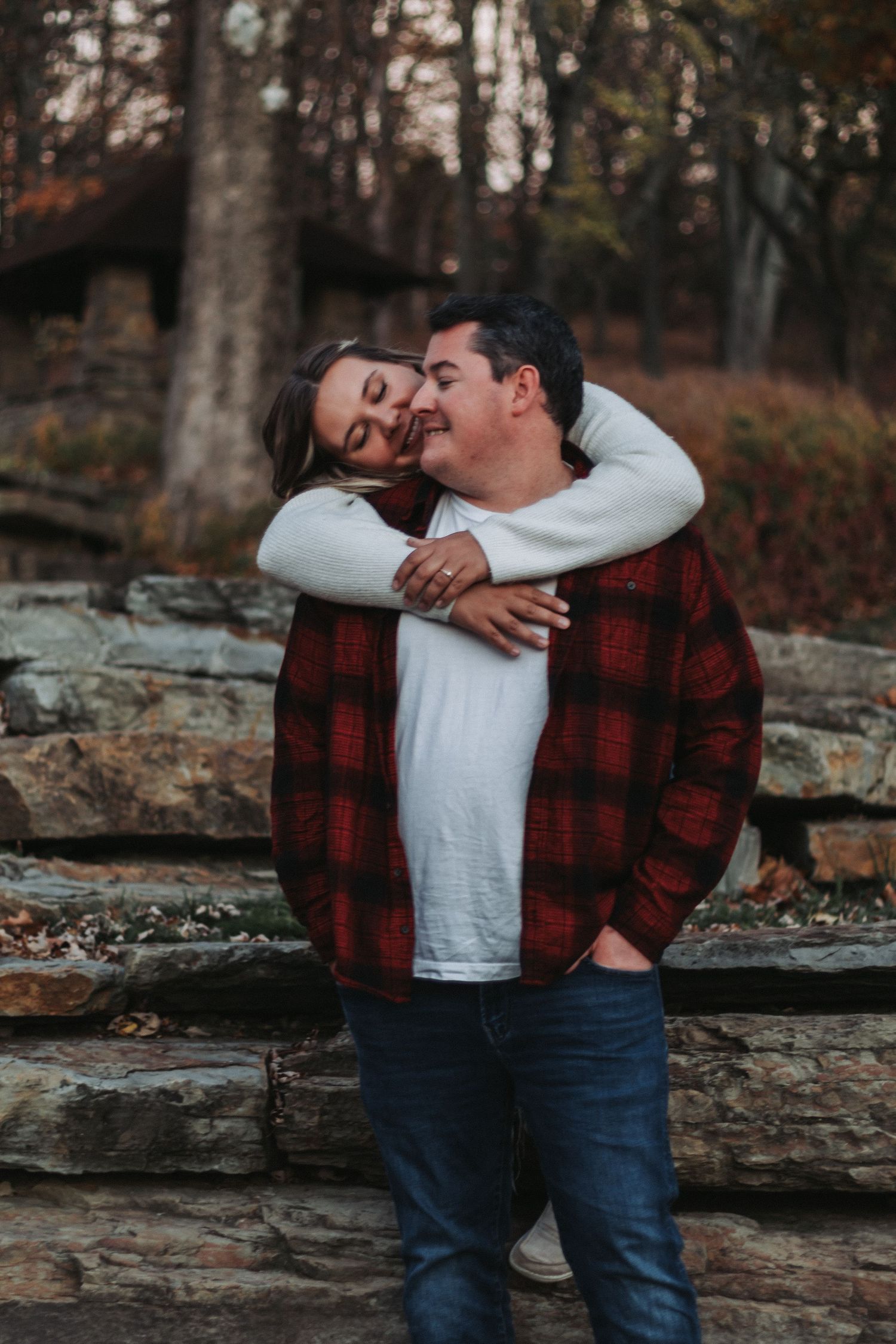 A playful embrace captured against a stone wall backdrop in autumn.