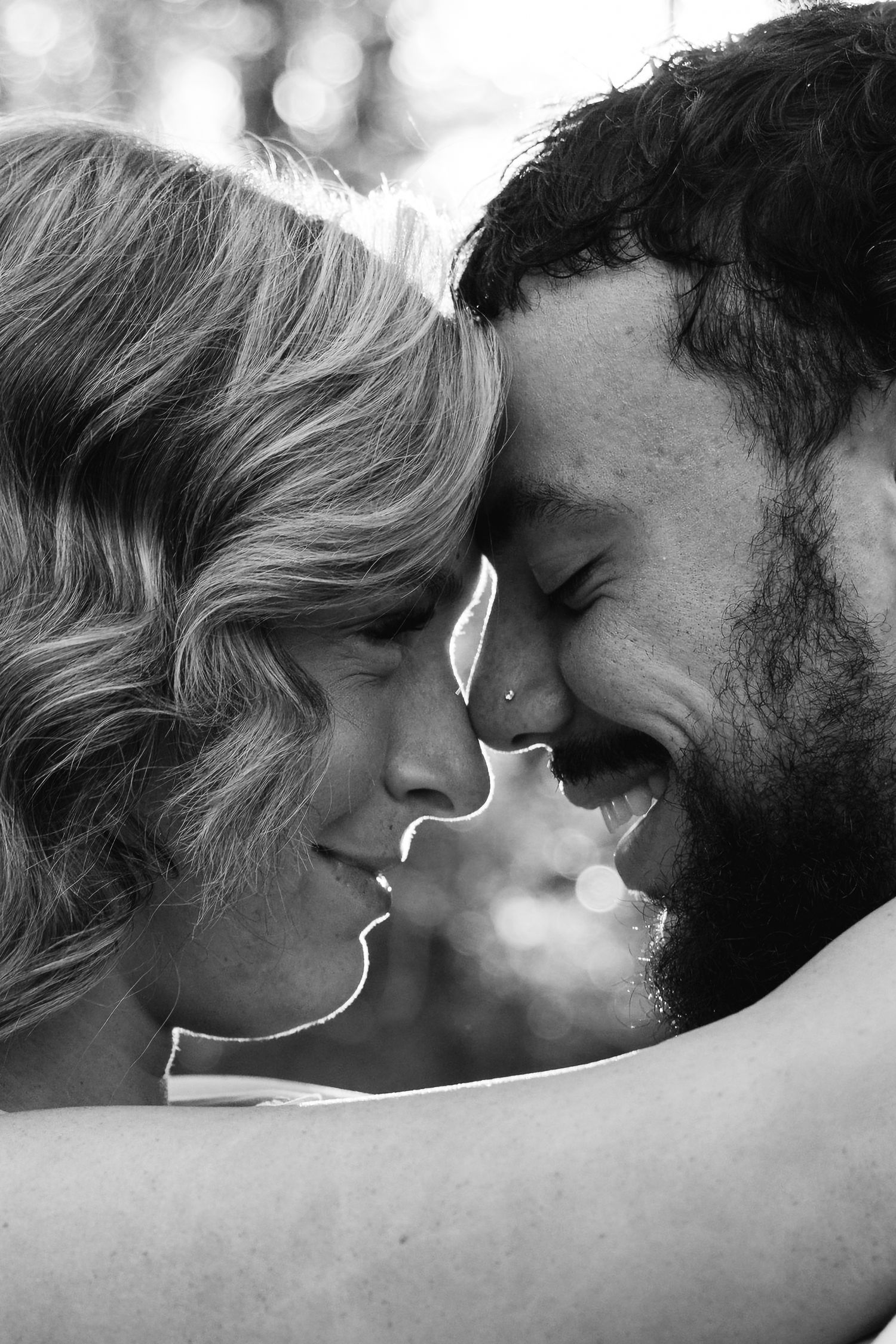 Black and white close-up of a smiling couple touching foreheads tenderly in an intimate romantic moment outdoors.