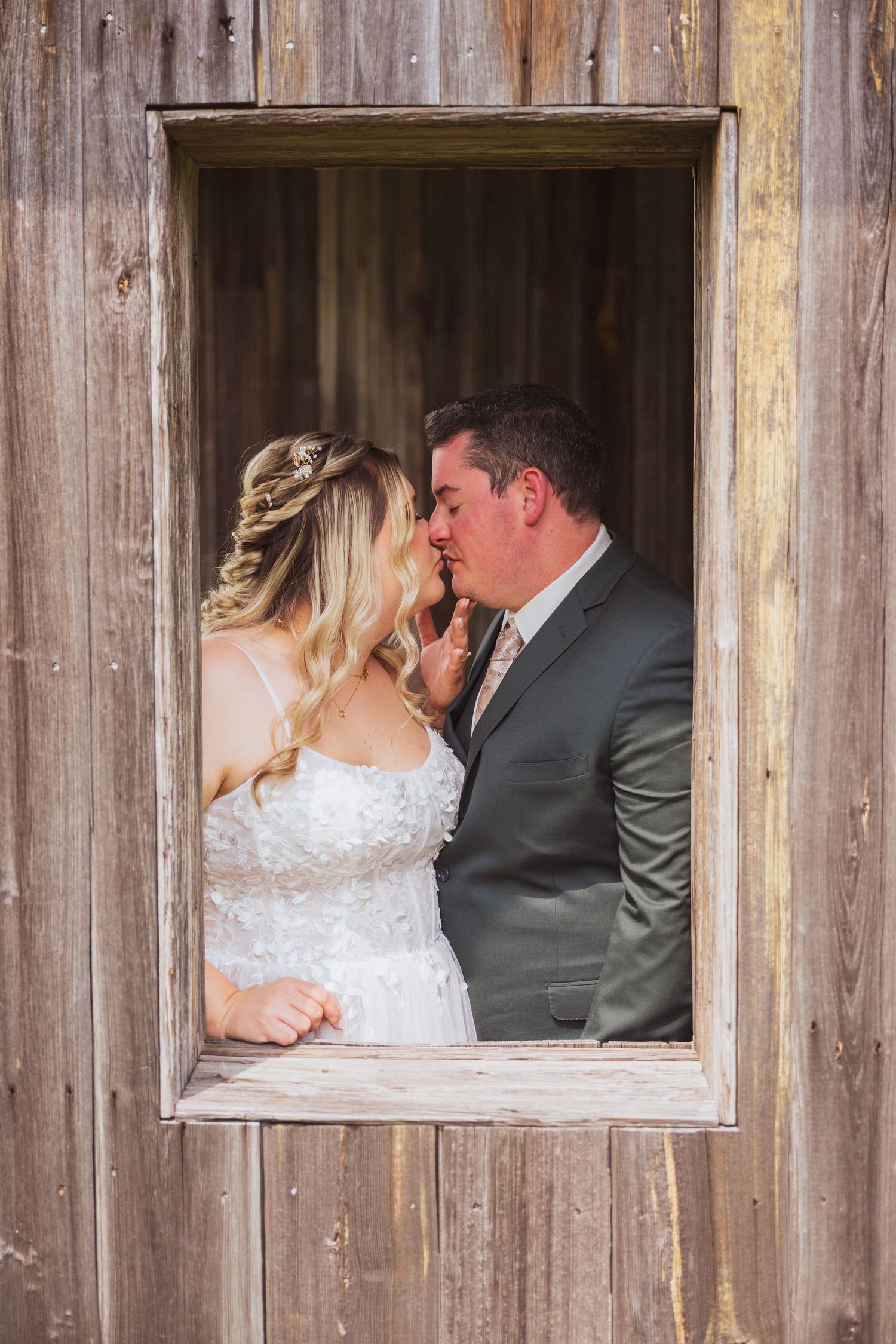 Intimate wedding moment captured through a rustic wooden window frame.
