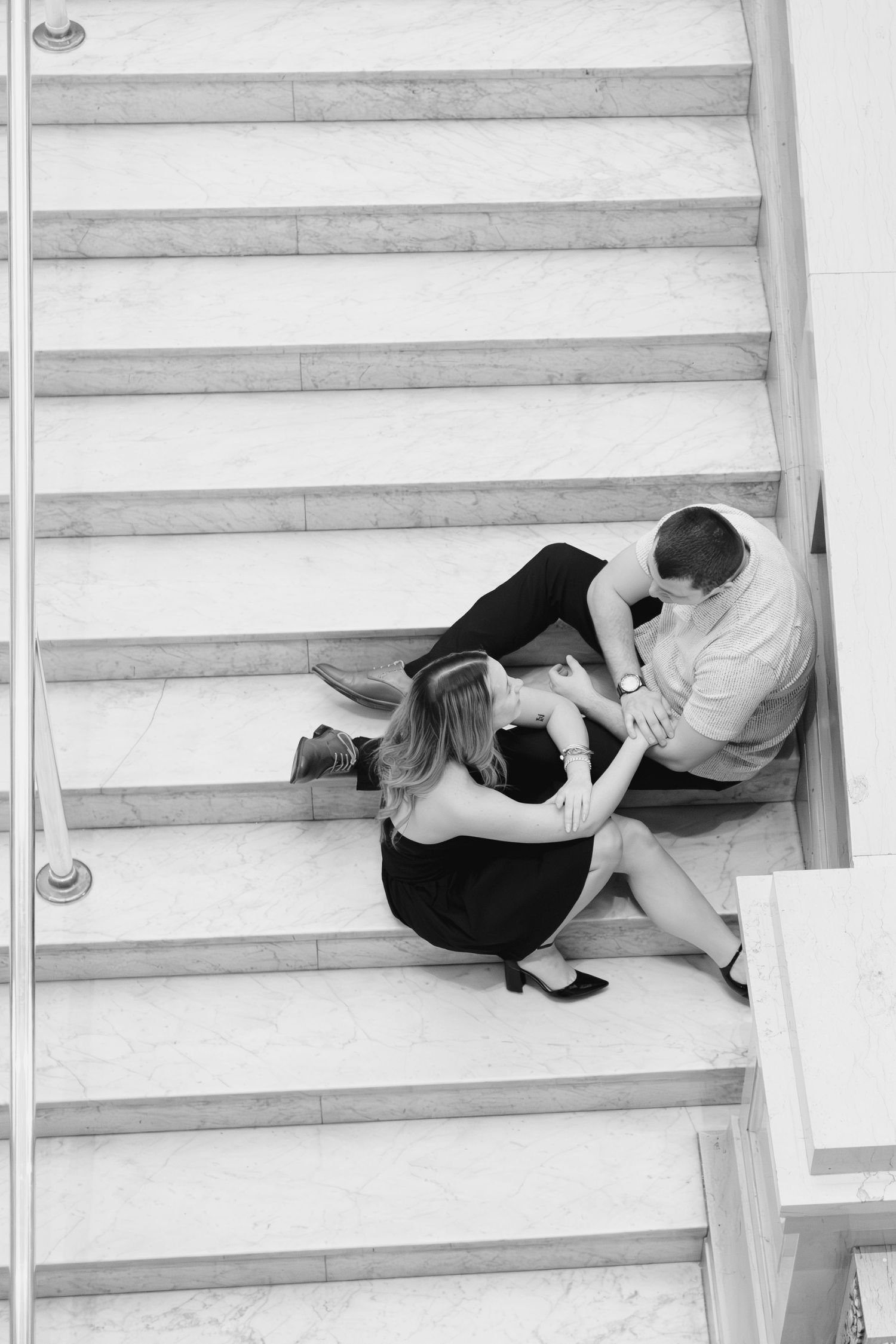 Black and white photo of couple sitting intimately on modern staircase.