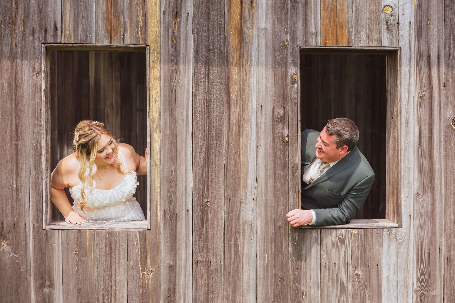 A playful wedding photo taken through two barn windows showing the couple peeking at each other.