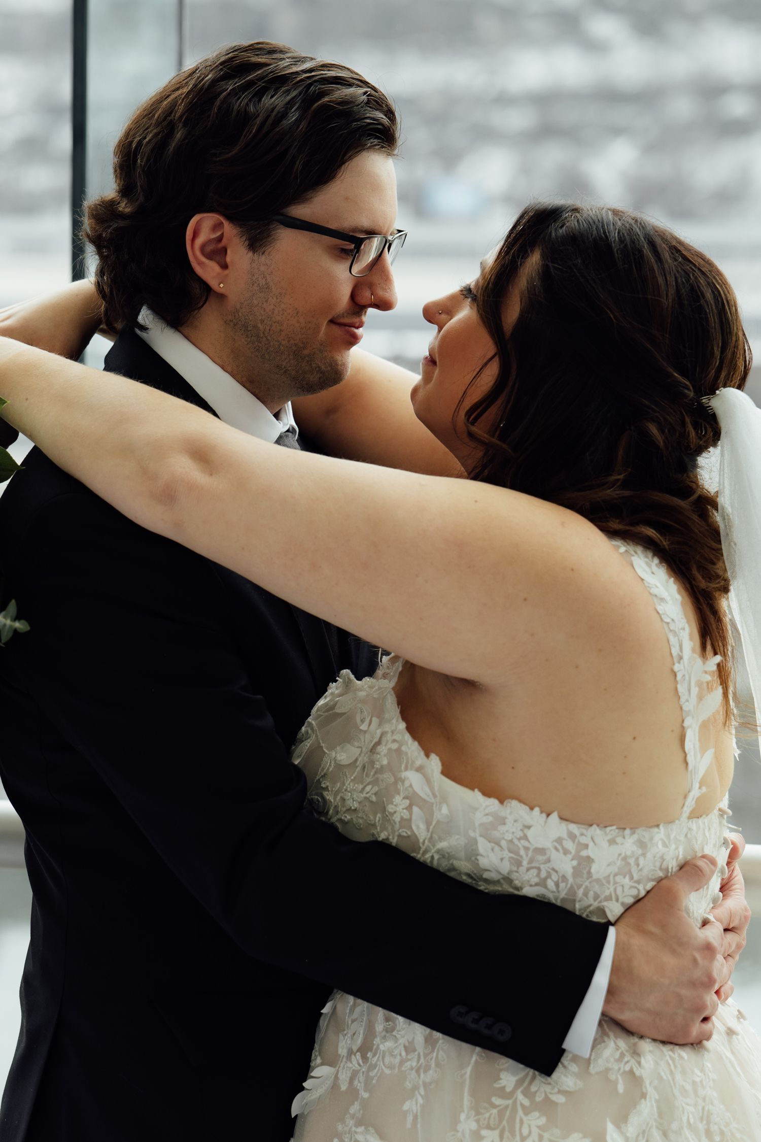 Bride and groom share an intimate first dance moment, bride in lace gown, groom in black tuxedo with glasses.